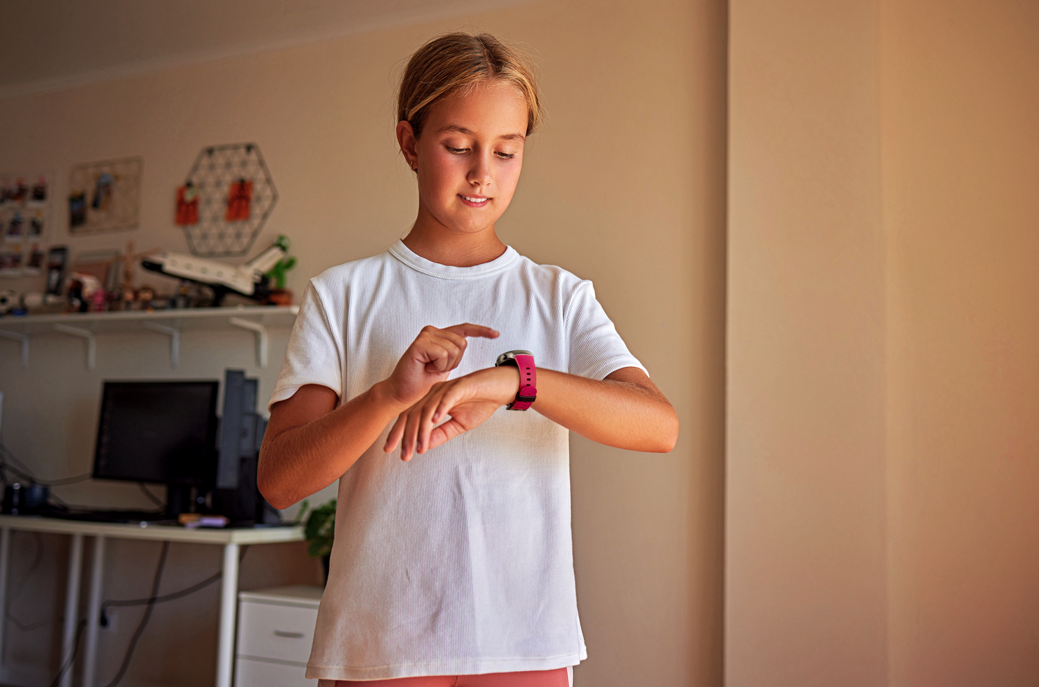 Una chica señala su reloj inteligente. Lleva una camisa blanca, reloj con correa rosa.