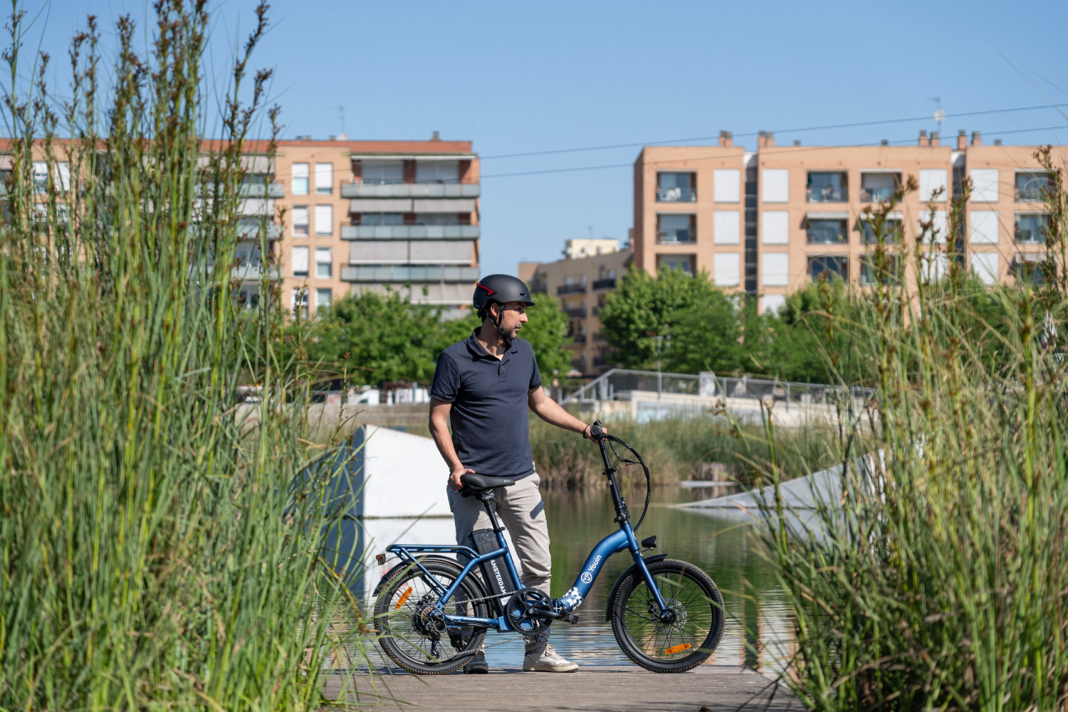 Hombre con casco de pie junto a una e-bike azul en un muelle de madera.