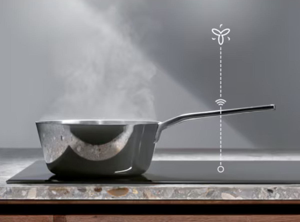 Srebrny garnek na czarnej płycie indukcyjnej, z unoszącą się parą i symbolem Wi-Fi nad nim.