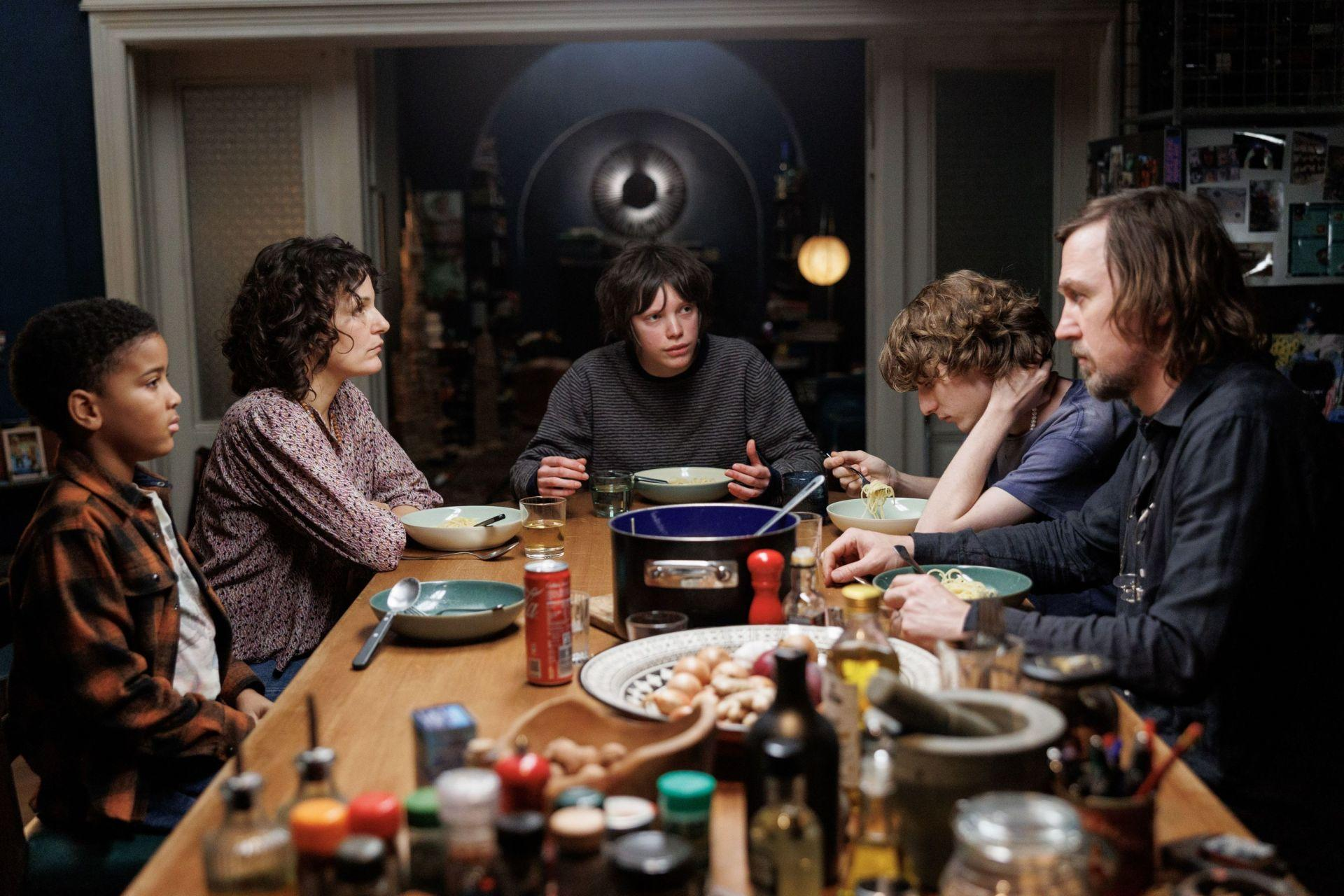 Familie am Tisch. Fünf Personen essen, dunkler Raum mit runder Lampe.