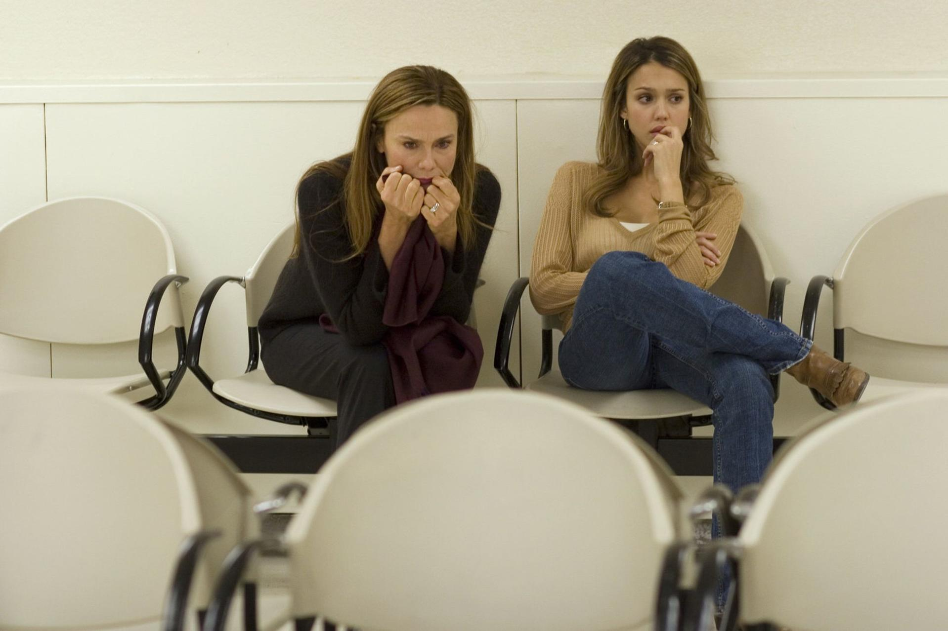 Zwei Frauen in Wartezimmer, besorgt, halten sich den Mund zu.
