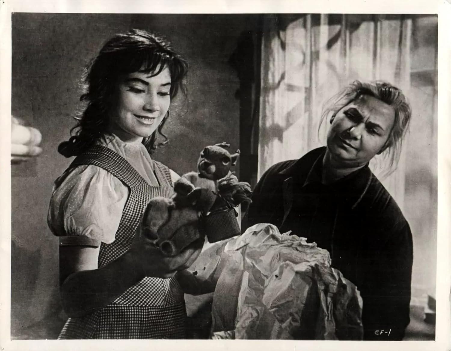 Frau hält Puppen, eine andere Frau schaut zu, in Schwarzweiß-Filmstill.