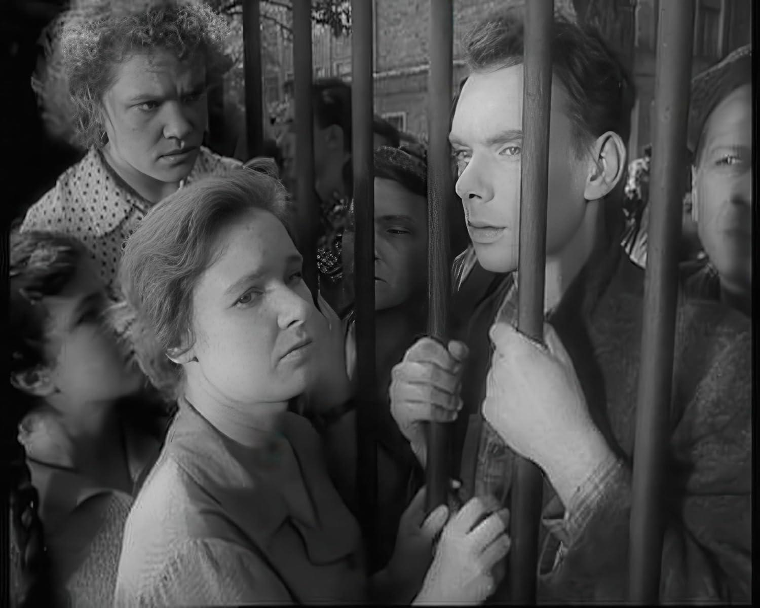 Menschen hinter Gittern, blicken auf andere, in einem Schwarzweiß-Filmstill.