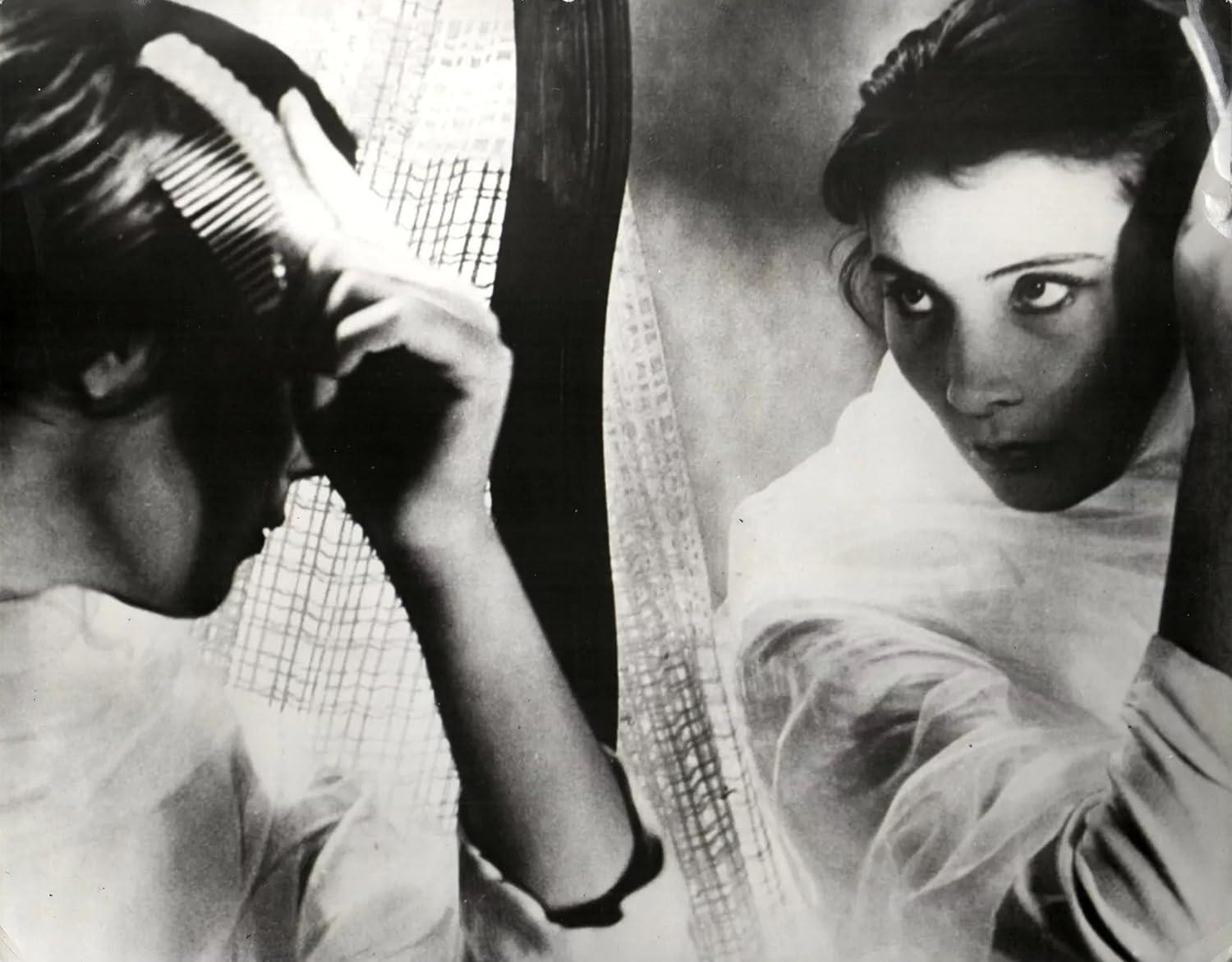 Frau kämmt sich die Haare im Spiegel, in einem Schwarzweiß-Filmstill.