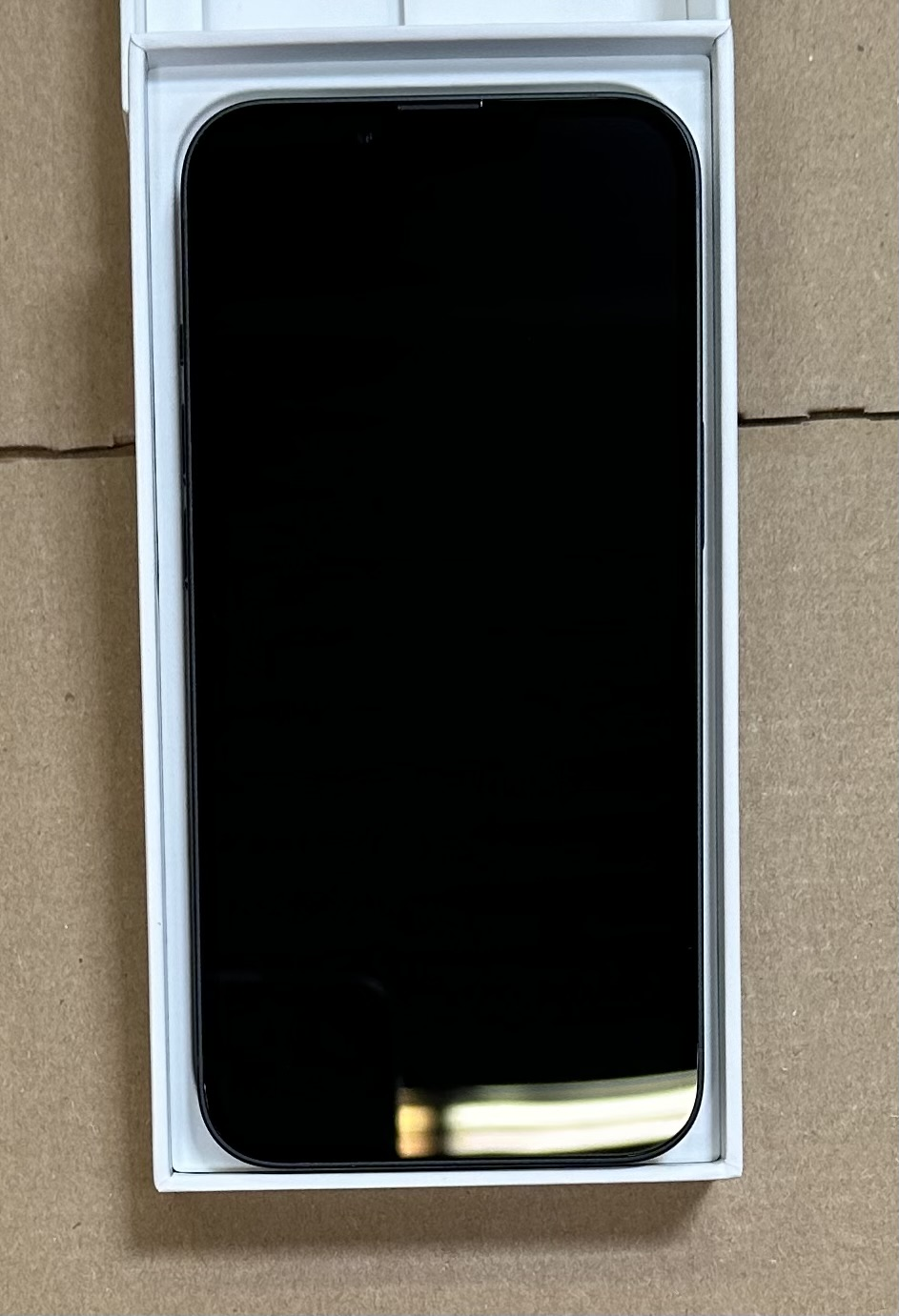 Czarny smartfon w białym pudełku na brązowym kartonie. Ekran jest ciemny i odbijający światło.