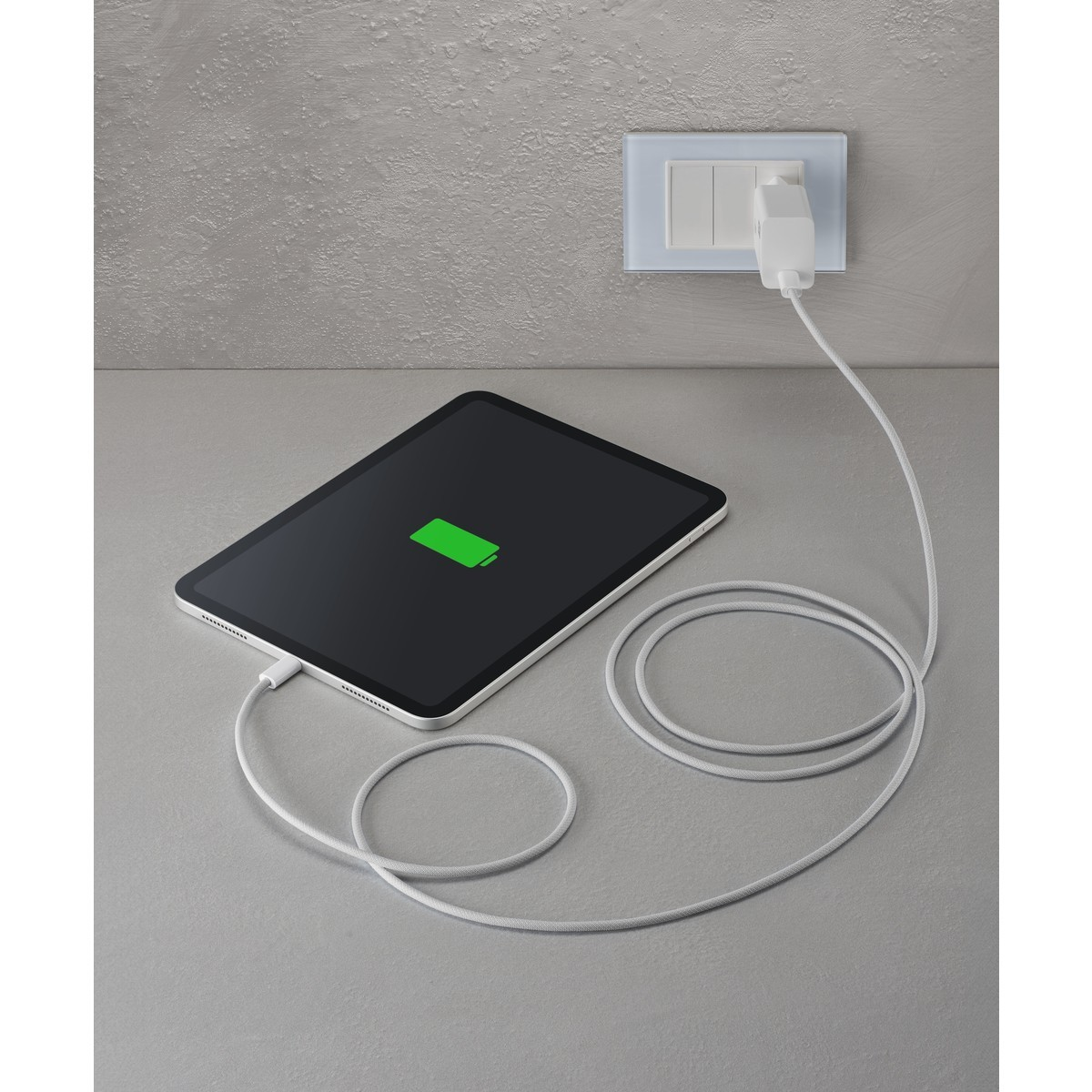 Tablet wird aufgeladen, an eine Steckdose angeschlossen. Das Tablet zeigt eine grüne Batterieanzeige. Das Kabel ist weiß.