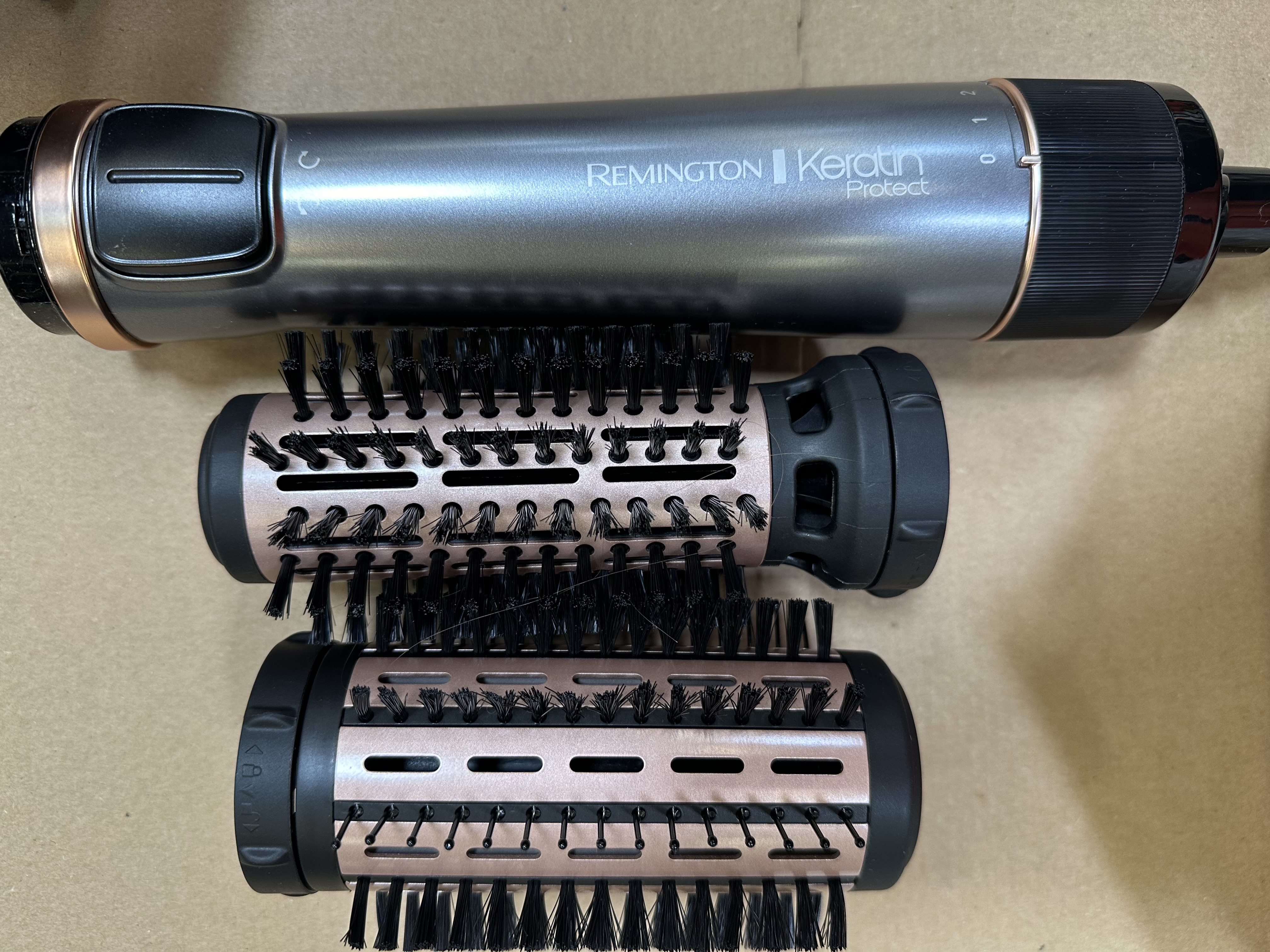 Zbliżenie stylizatora do włosów Remington. Widoczne urządzenie i nasadki. Czarny i złoty.