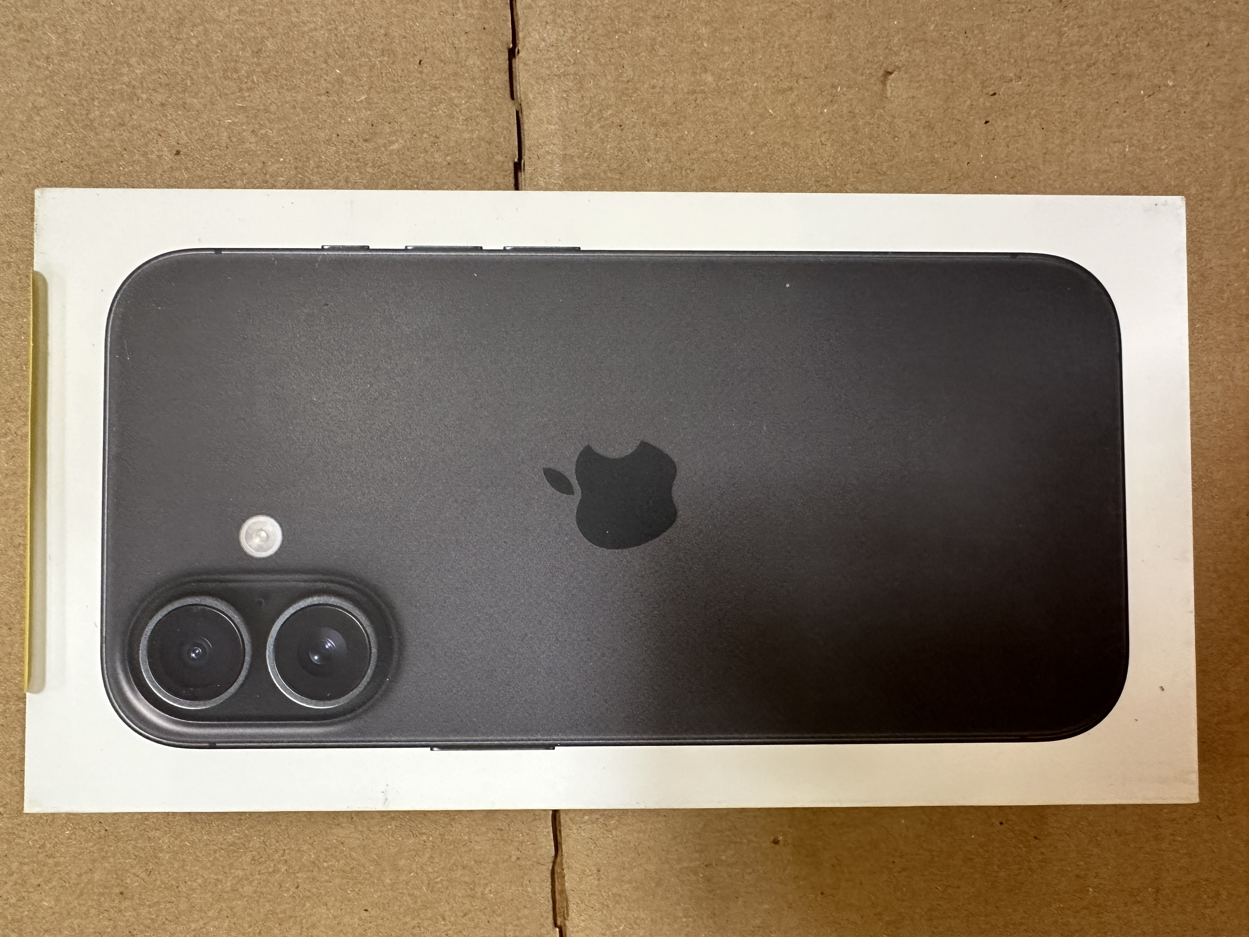 Czarny smartfon w białym pudełku. Logo Apple z tyłu. Tło z kartonu.