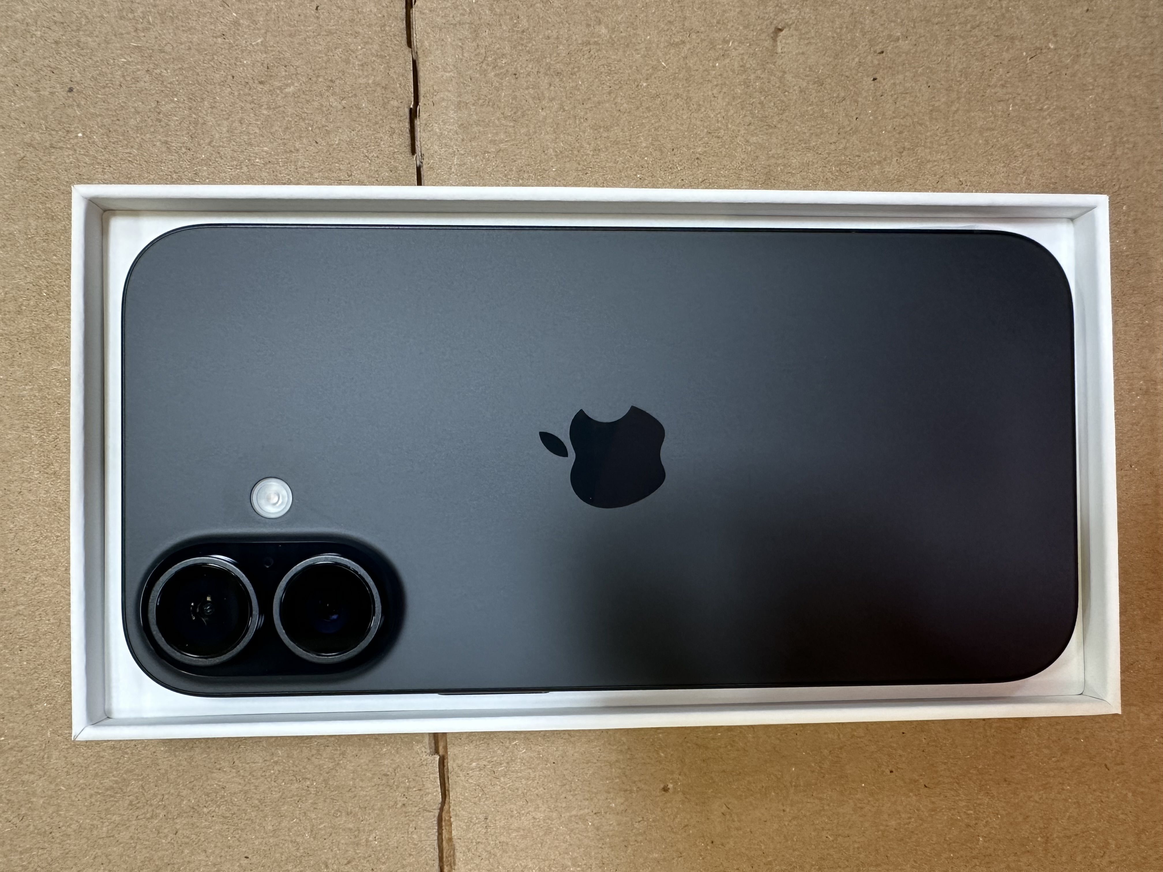 Zbliżenie na tył czarnego smartfona w pudełku. Widoczne logo Apple i aparat fotograficzny.