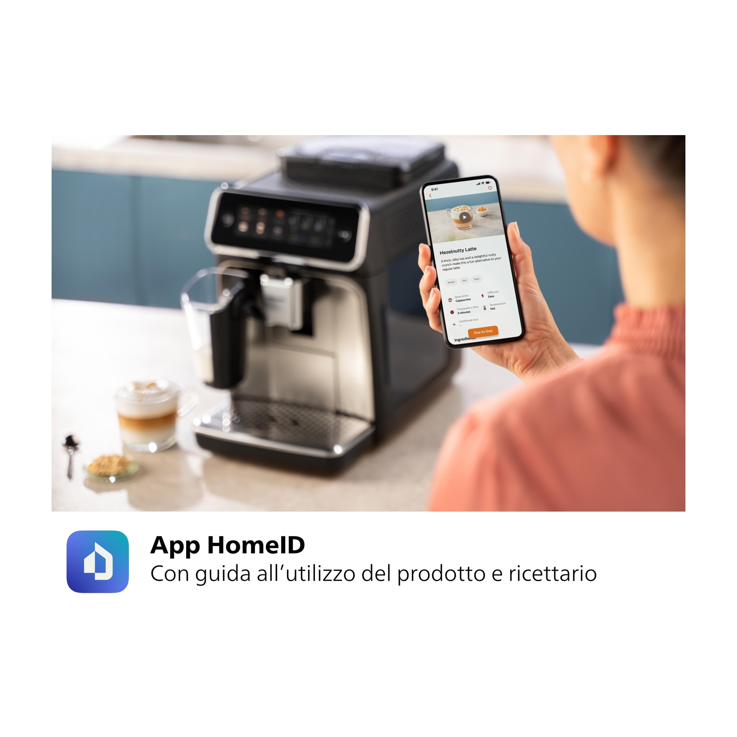 Una persona tiene in mano un telefono che mostra l'app della macchina da caffè. Macchina e tazza visibili.