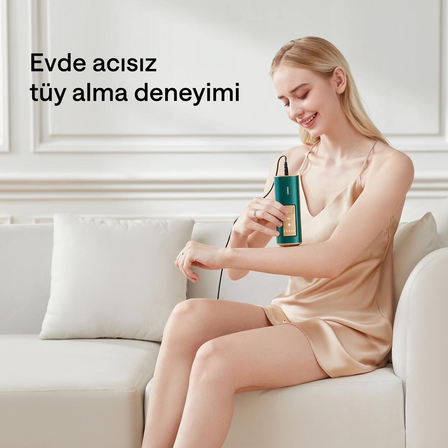Sarışın bir kadın kanepede oturuyor, kolunda yeşil bir tüy alma cihazı kullanıyor.