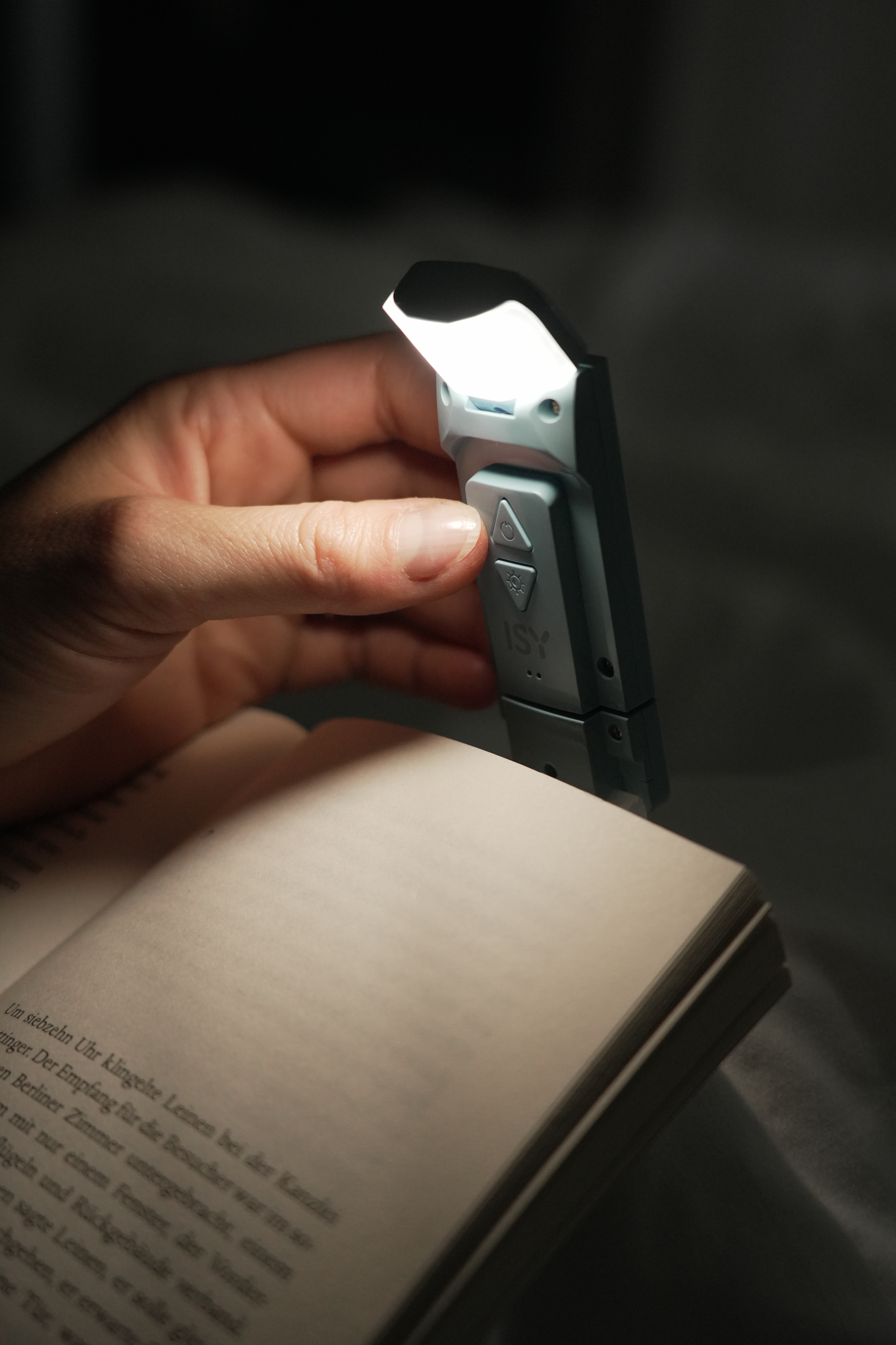 Une main tenant un livre avec une lampe de lecture sur la page.