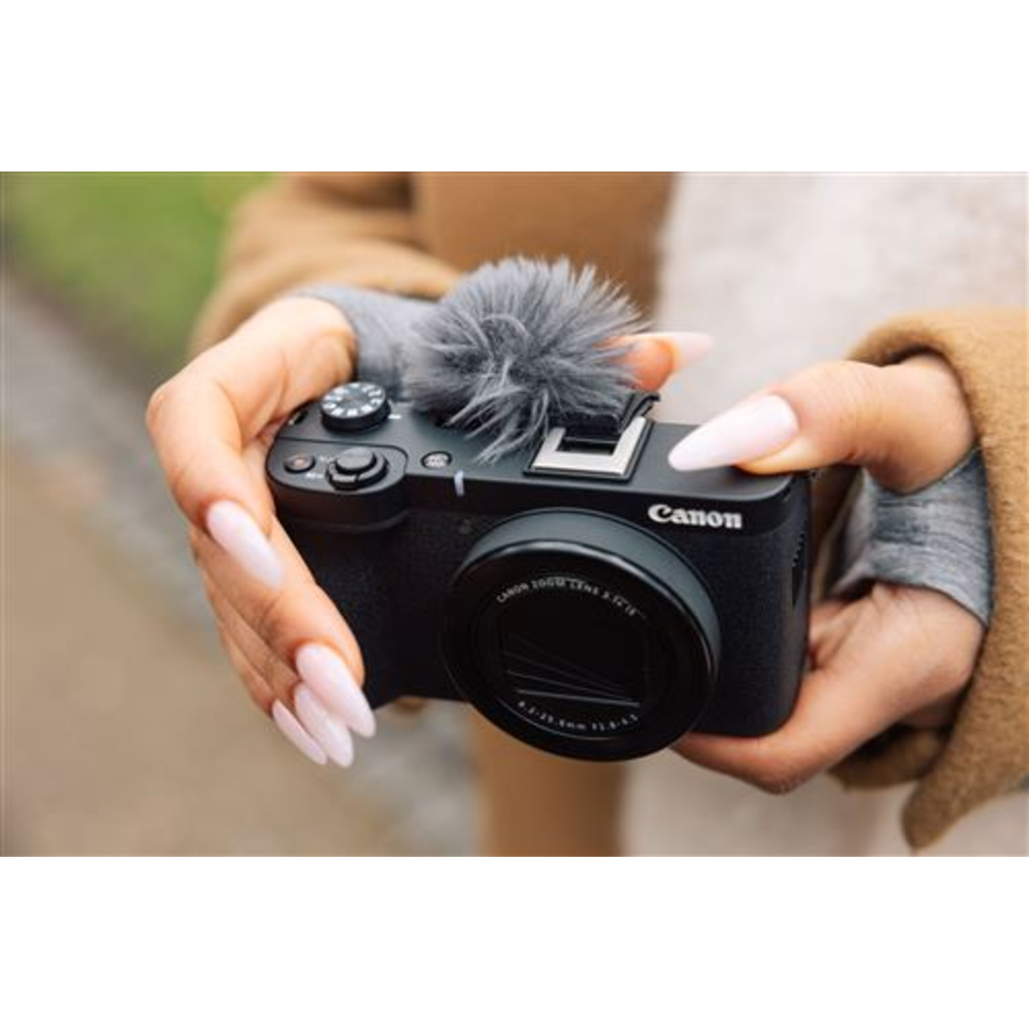 Hands holding black camera with microphone, outdoors. Long nails.