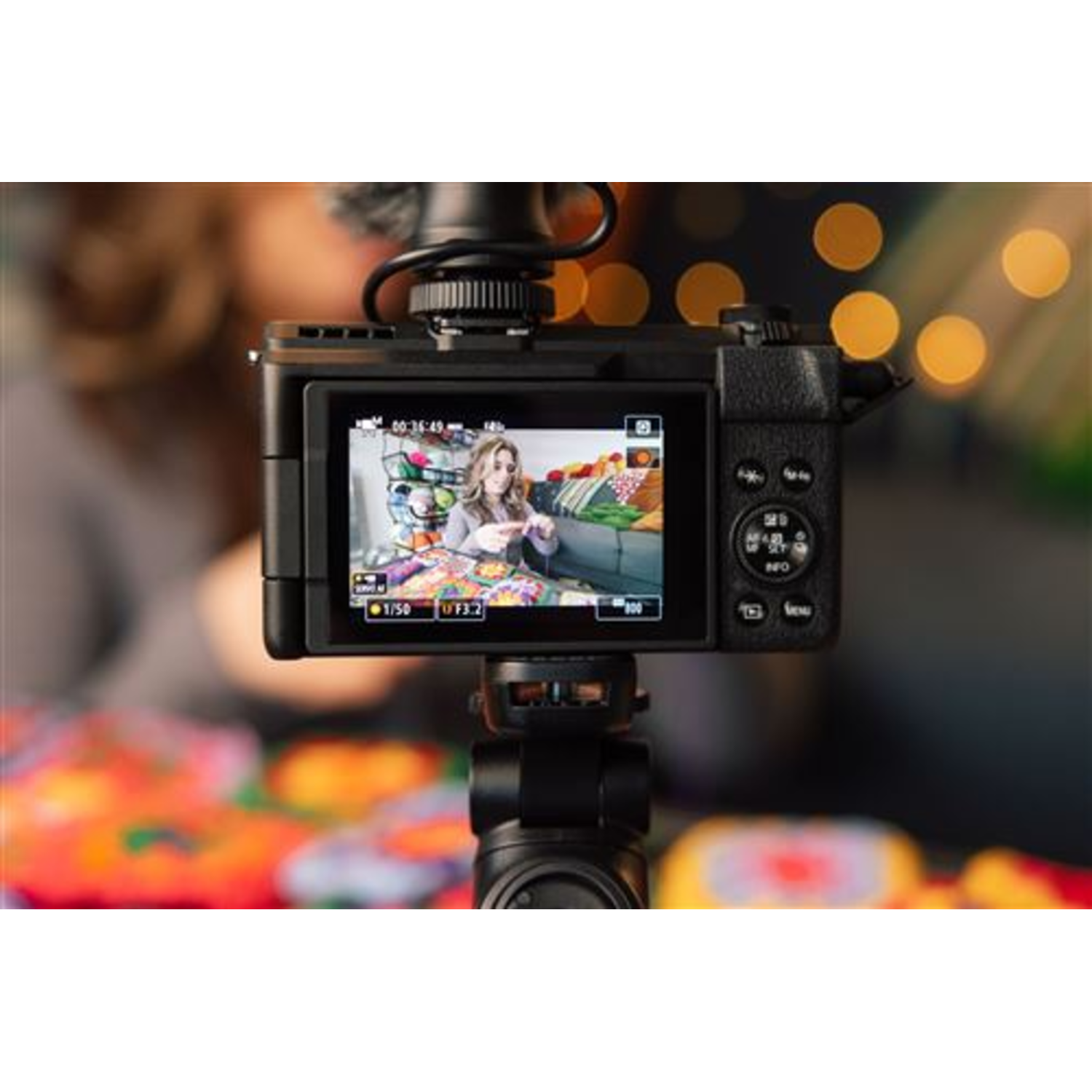 Camera showing a woman on the screen, on a tripod. Colorful objects in the background.