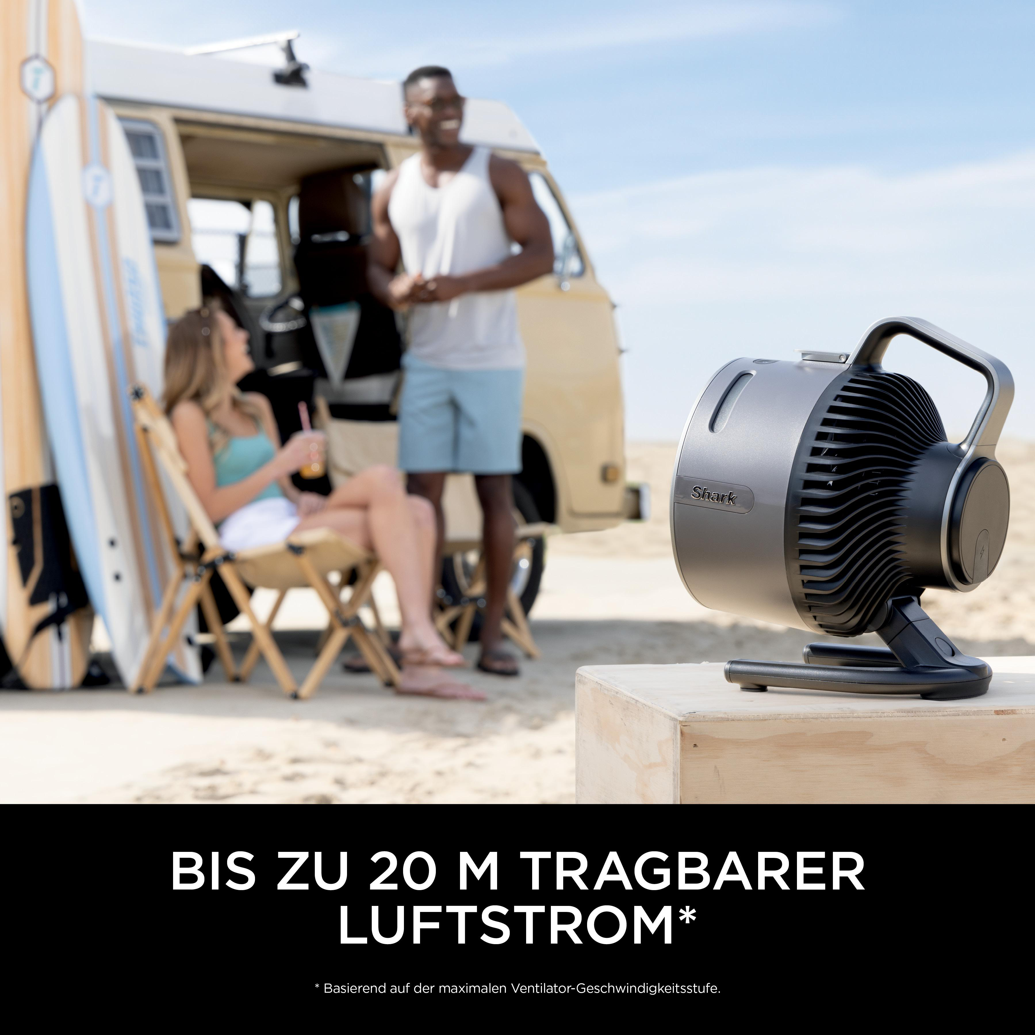 Schwarzer Ventilator auf einer Holzkiste mit zwei Personen und Surfbrettern im Hintergrund.