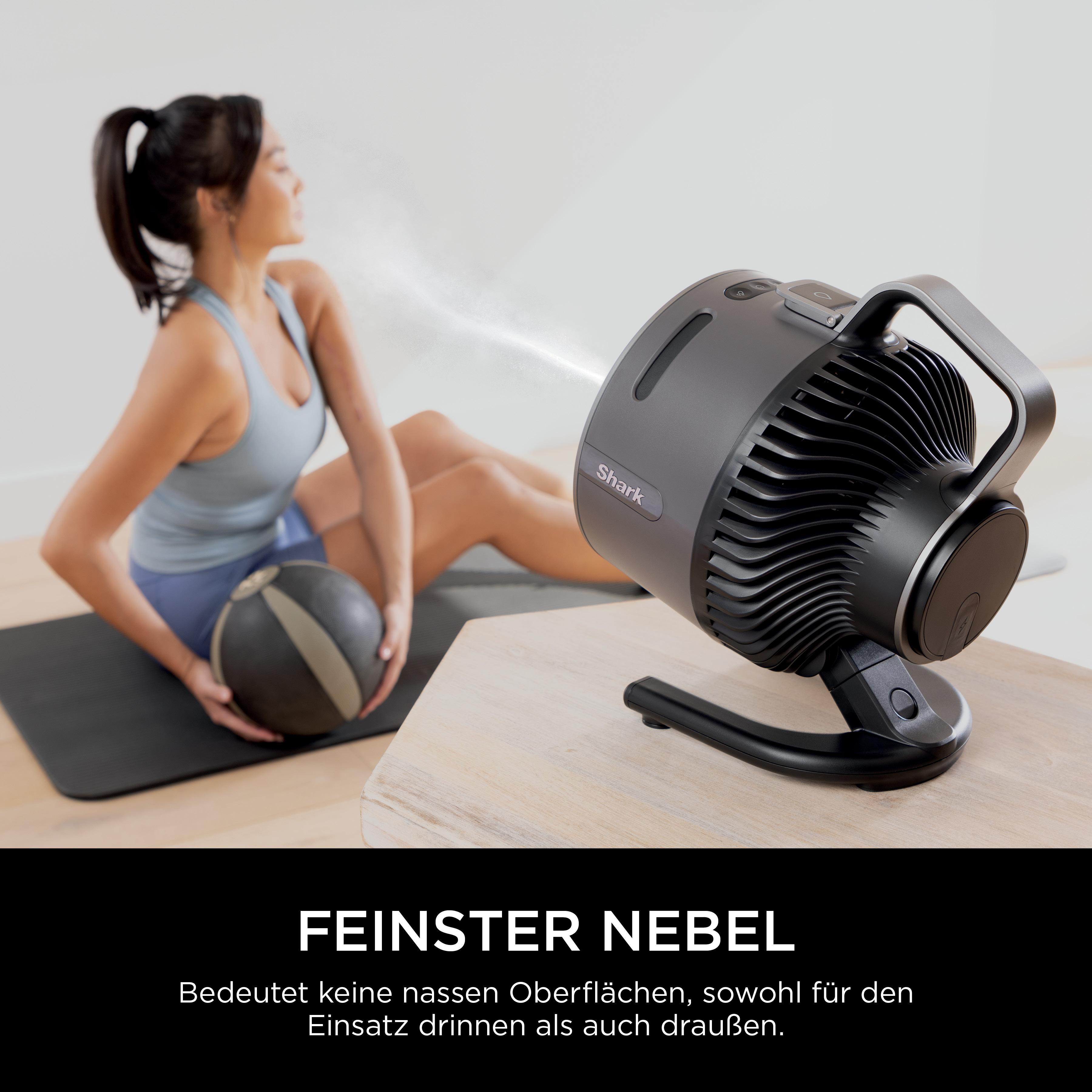 Schwarzer Ventilator mit Dunst auf einem Tisch neben einer sitzenden Person.