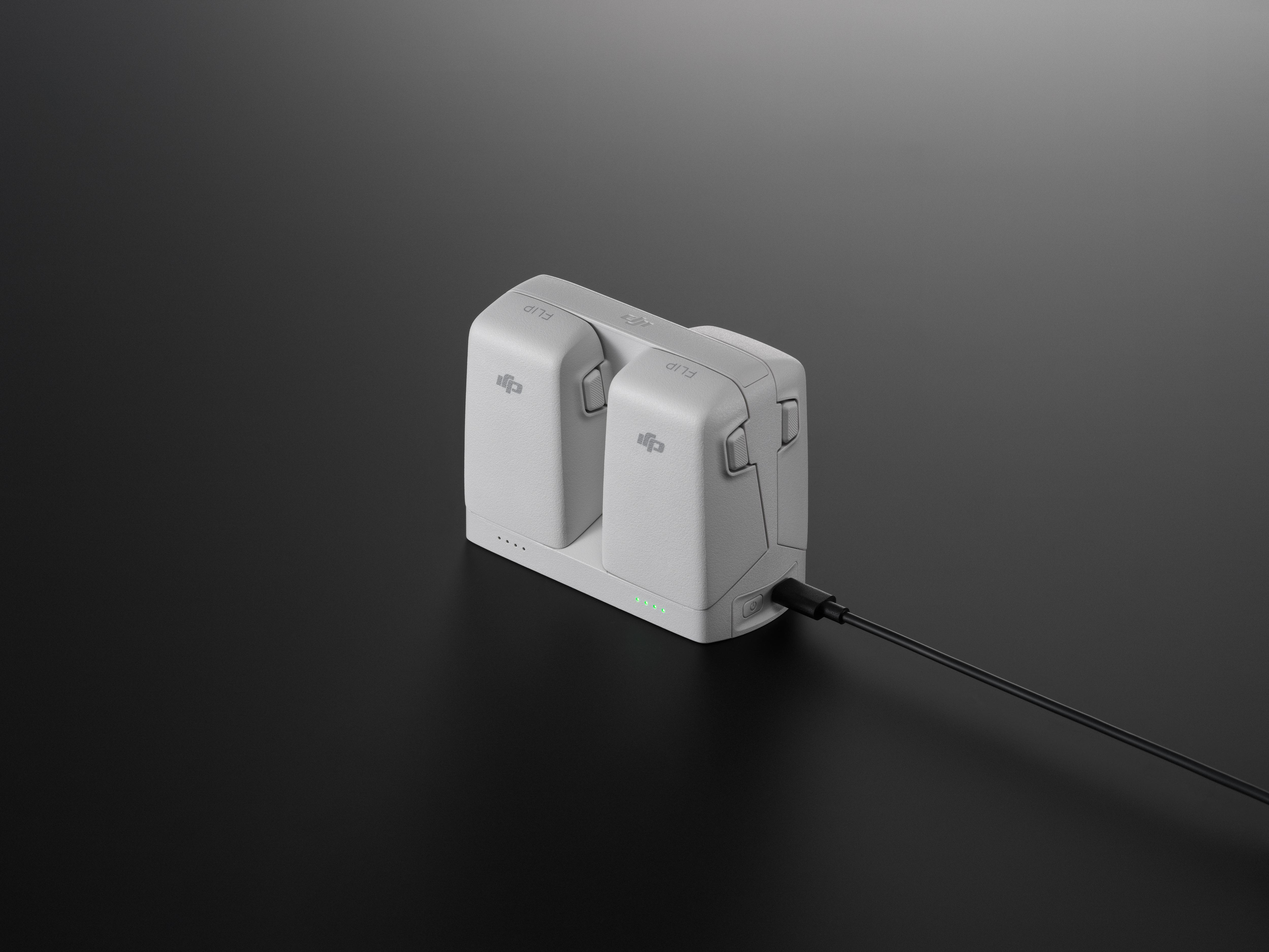 Weißes Drohnen-Batterieladegerät mit zwei Schlitzen, einem schwarzen Kabel und einer dunklen Oberfläche.