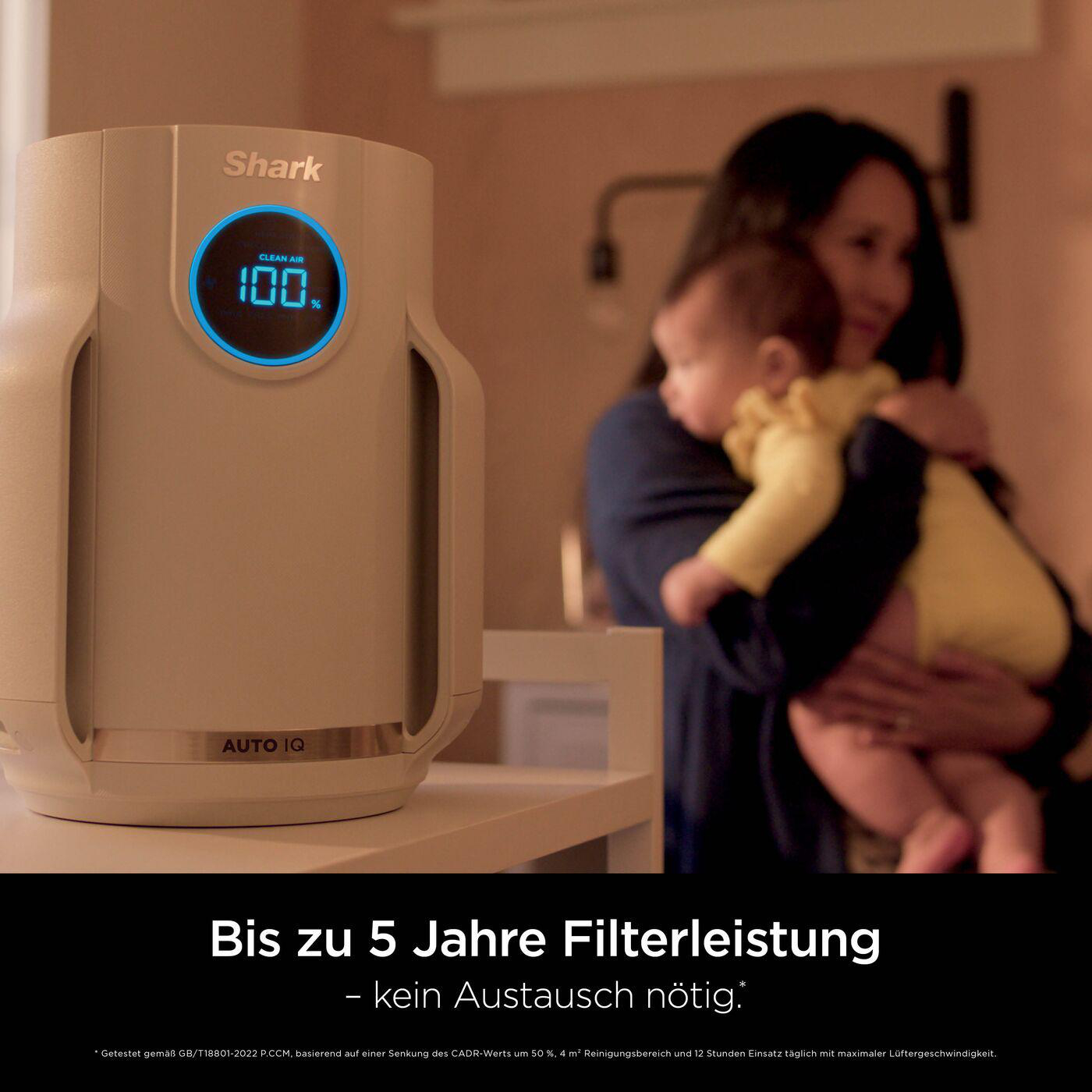 Frau hält Baby, Luftreiniger im Hintergrund. Anzeige 100% saubere Luft. Sanfte Beleuchtung, häusliche Umgebung.