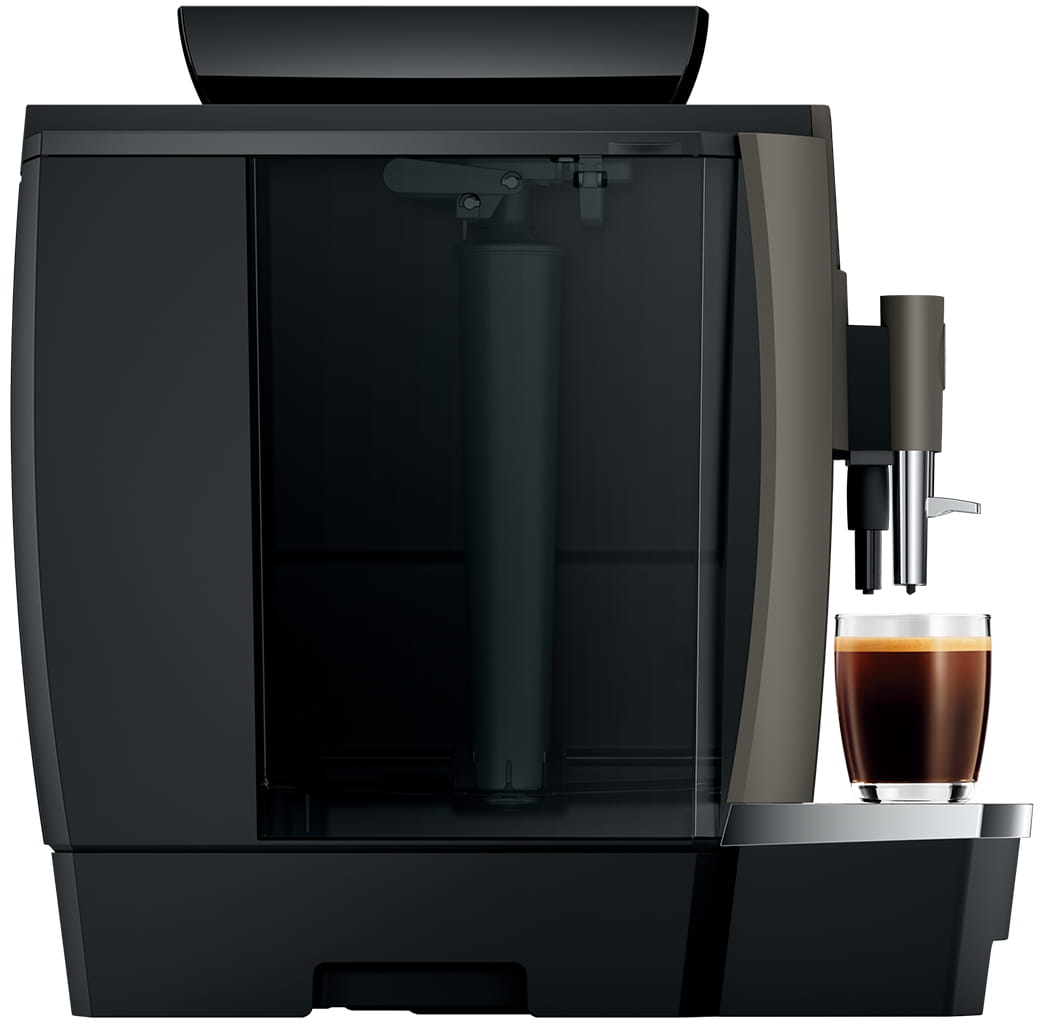 Macchina da caffè scura, vista laterale, con bicchiere di caffè. Base nera, serbatoio acqua trasparente.
