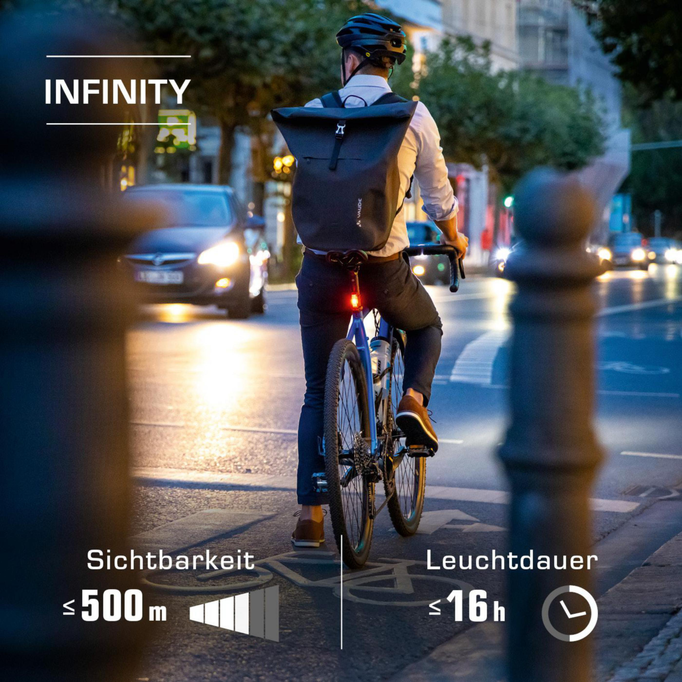 Radfahrer fährt nachts Fahrrad. Fahrrad hat rotes Rücklicht. Straßenszene.