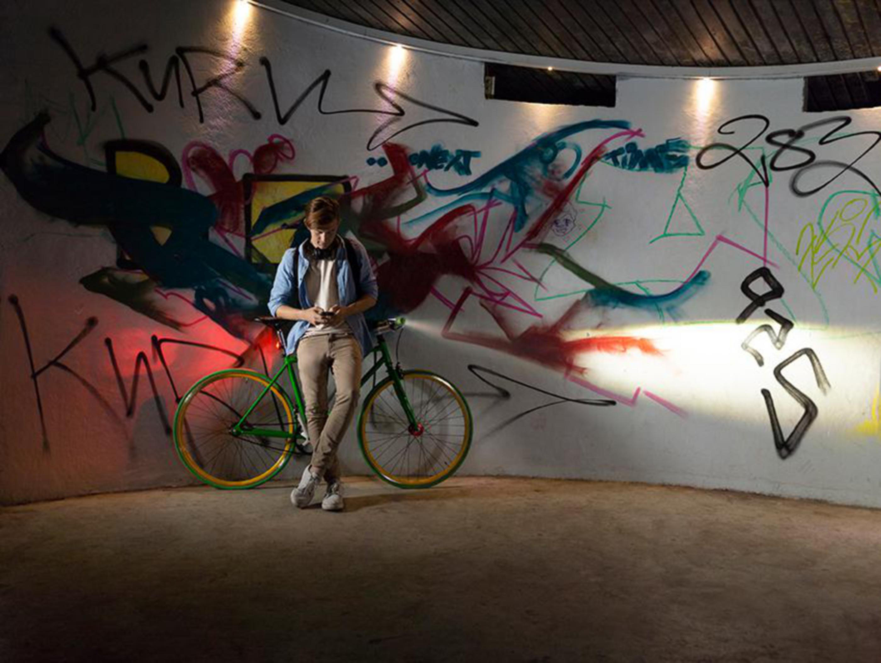 Ein Mann lehnt an einem Fahrrad und textet. Graffiti-Wand im Hintergrund.
