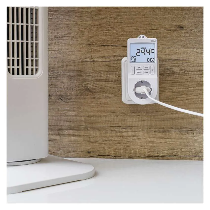 Egy fehér digitális időzítő dugó a fali aljzatban egy ventilátoros fűtőtesttel az asztalon.