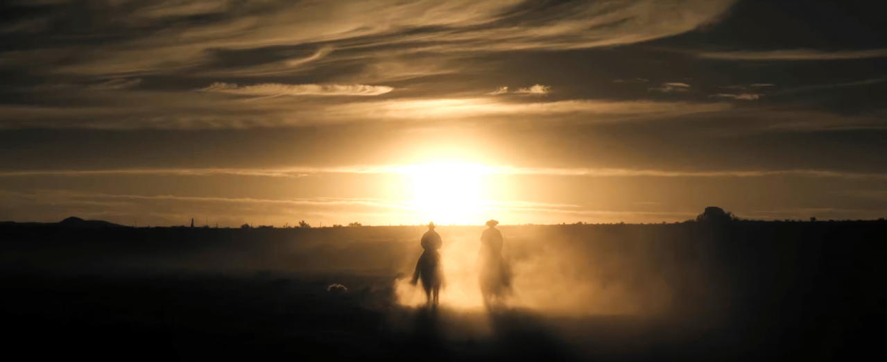 Zwei Cowboys auf Pferden vor Sonnenuntergang. Staub in der Luft.