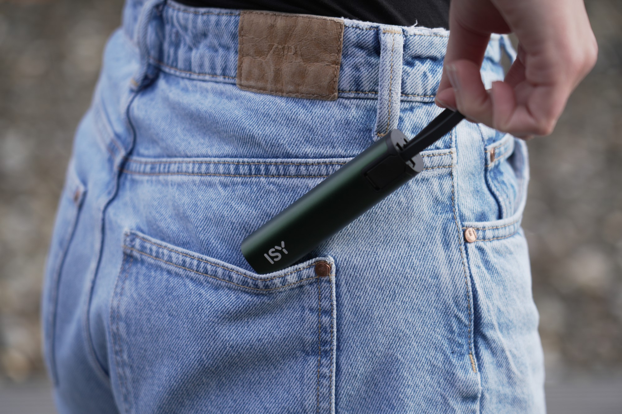 Ręka umieszczająca małe, ciemnozielone urządzenie ISY w kieszeni dżinsów z widocznym logo ISY.