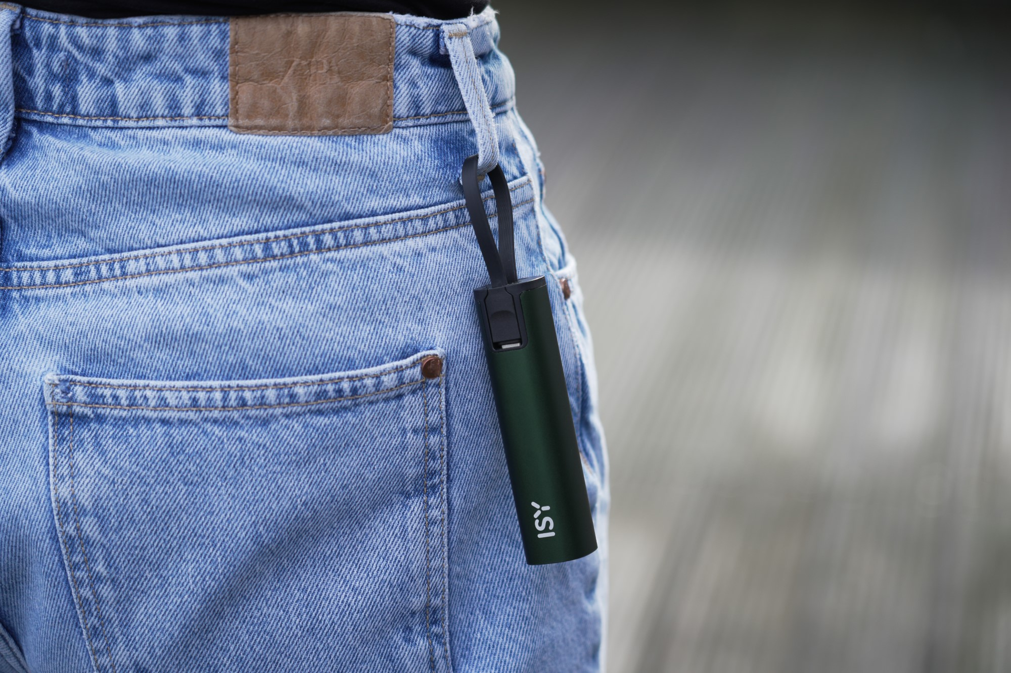 Ciemnozielone urządzenie ISY wiszące z kieszeni dżinsów na czarnym pasku.
