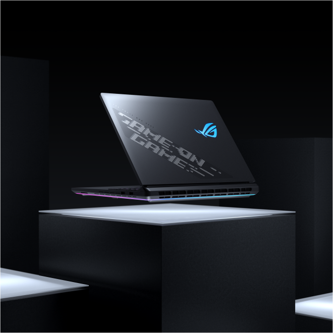Fekete laptop állványon, nyitott, Strix logó, megvilágított talp, fekete háttér.