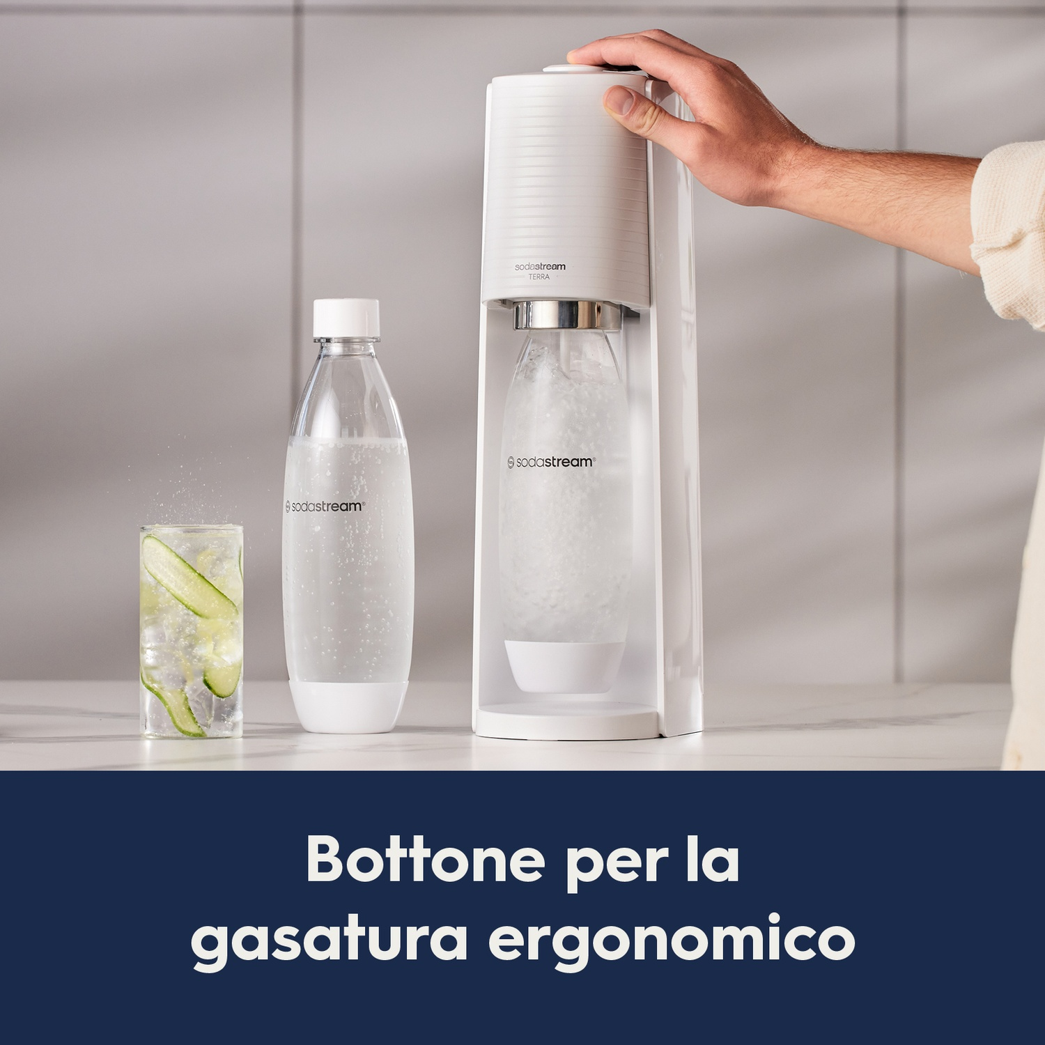 Una macchina SodaStream, una bottiglia e un bicchiere con fette di cetriolo, con testo: Pulsante di gasatura ergonomico.