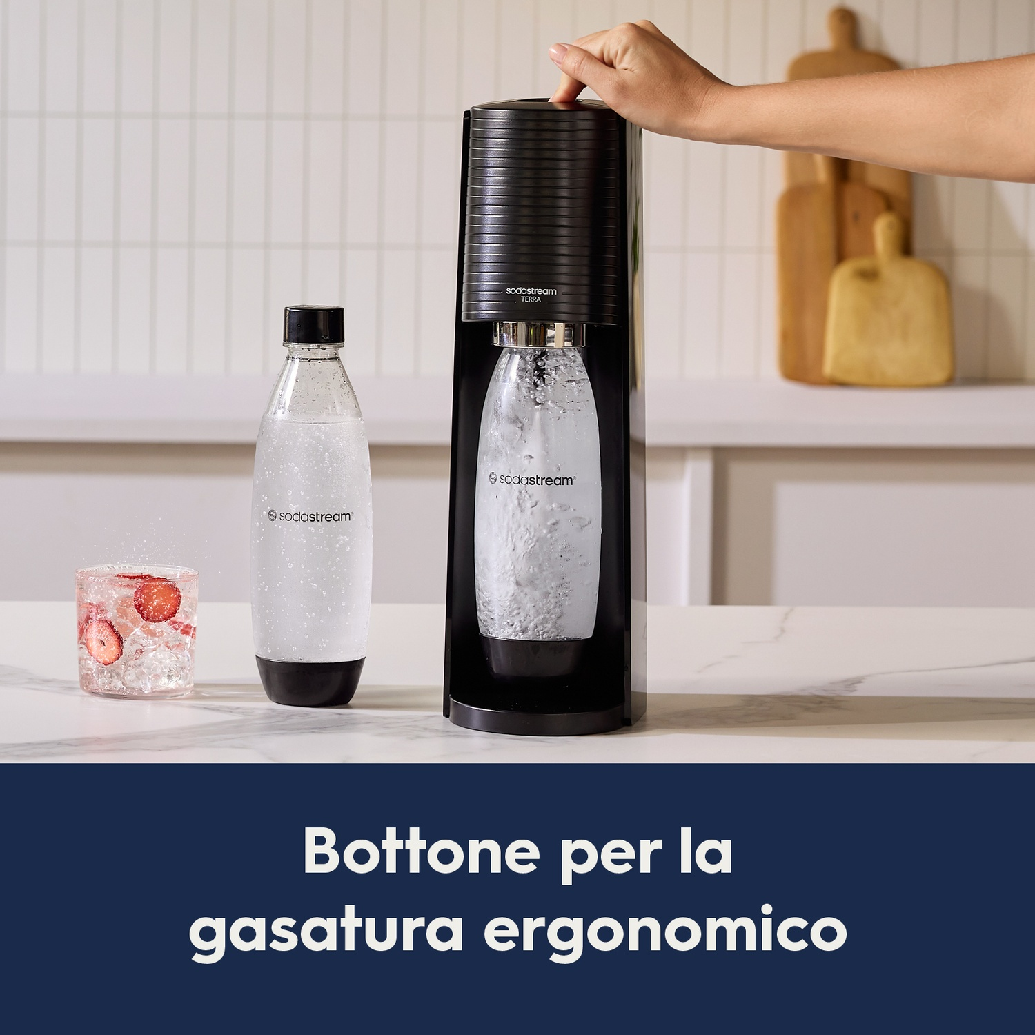 Una mano preme un pulsante su una macchina SodaStream, con una bottiglia e un bicchiere accanto.