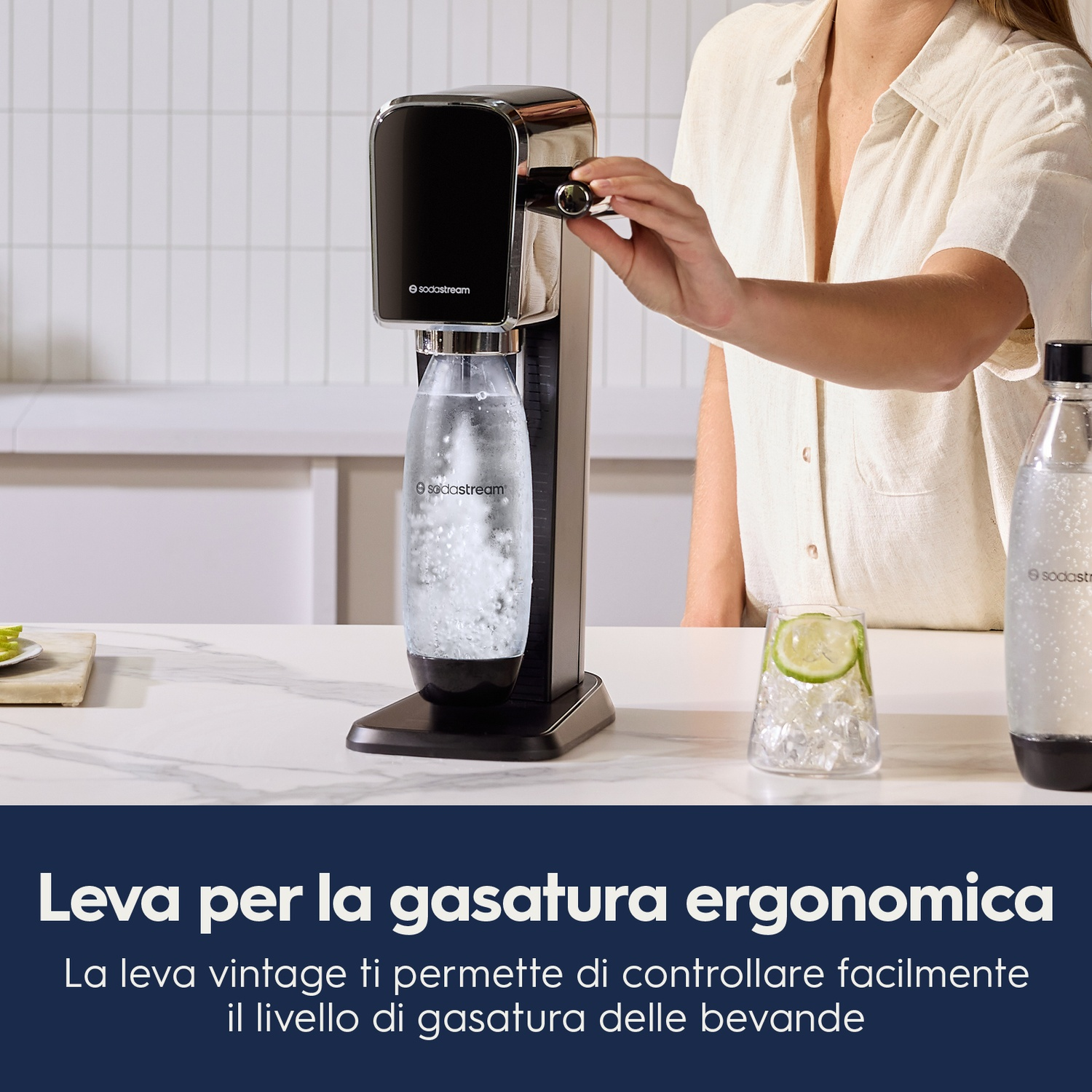 Una donna usa una macchina SodaStream, con un bicchiere e una bottiglia accanto, in cucina.