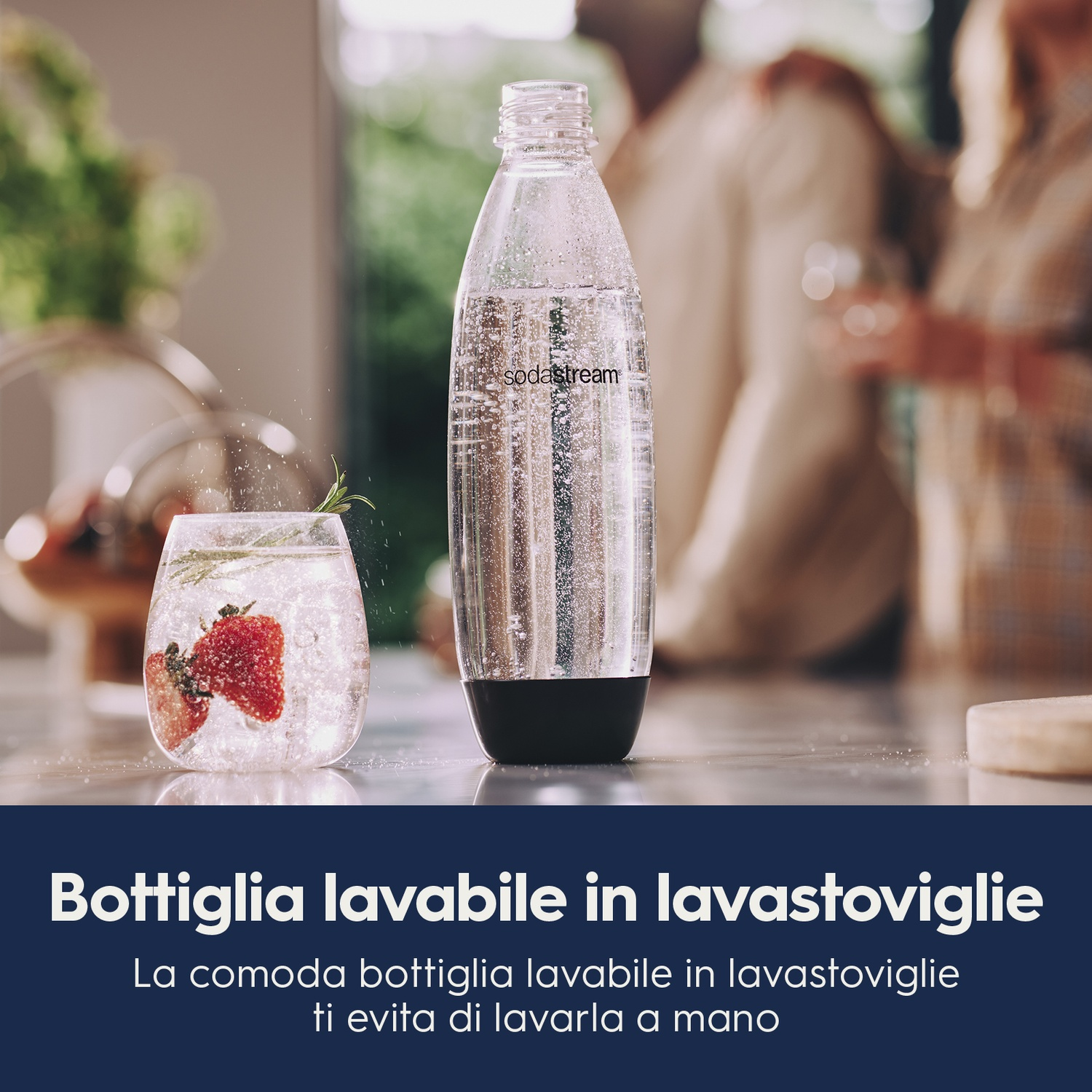 Una bottiglia trasparente e un bicchiere con fragole e ghiaccio. Dietro, una scena di cucina sfocata con persone.