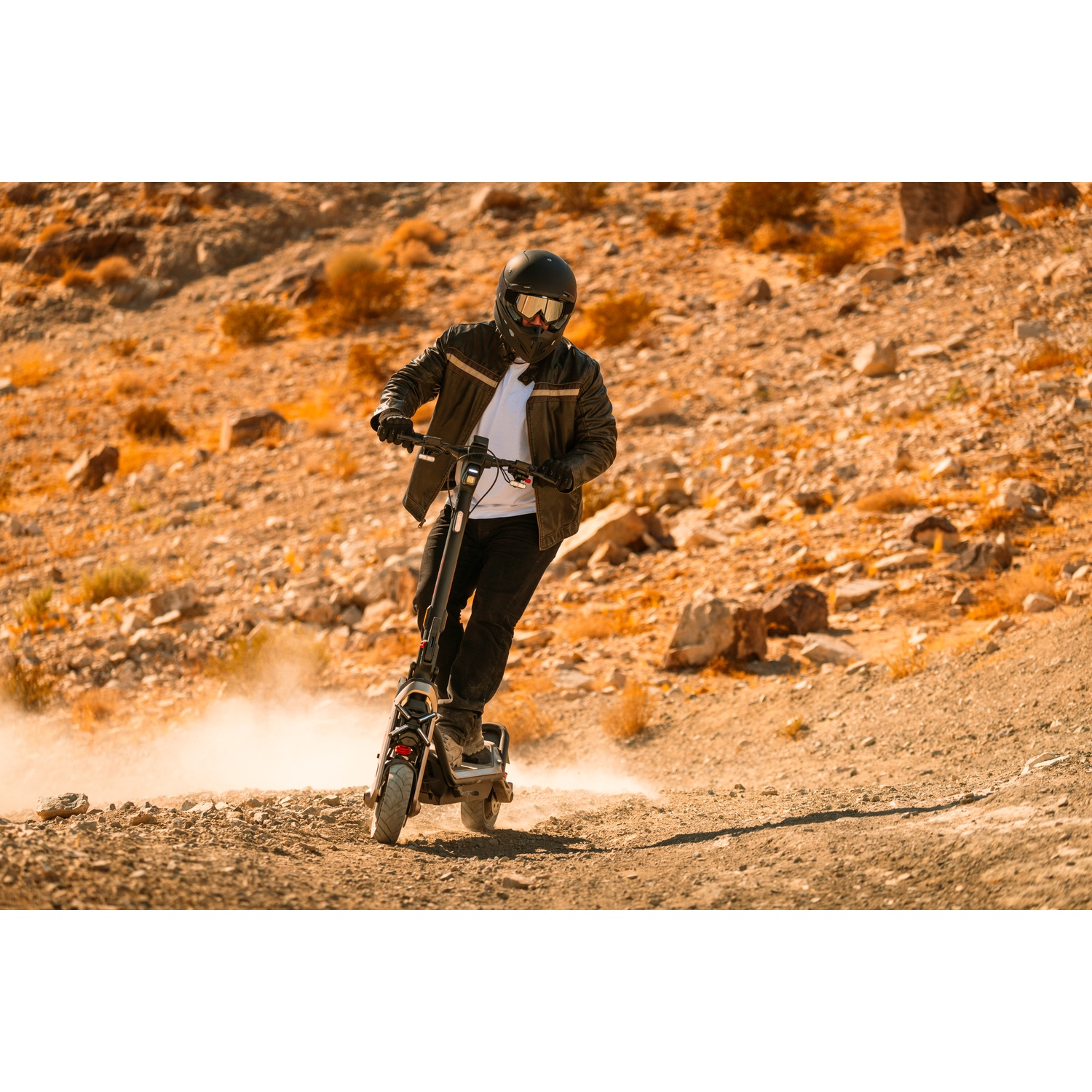 Persona che guida uno scooter elettrico su un sentiero sterrato nel deserto.