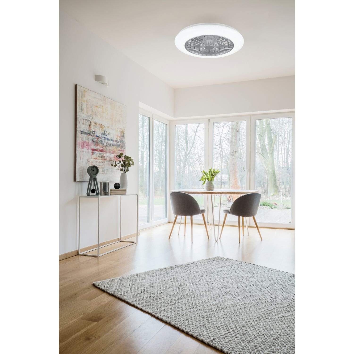 Una stanza interna con un ventilatore da soffitto, tavolo, sedie, opere d'arte e tappeto, vicino a una finestra.
