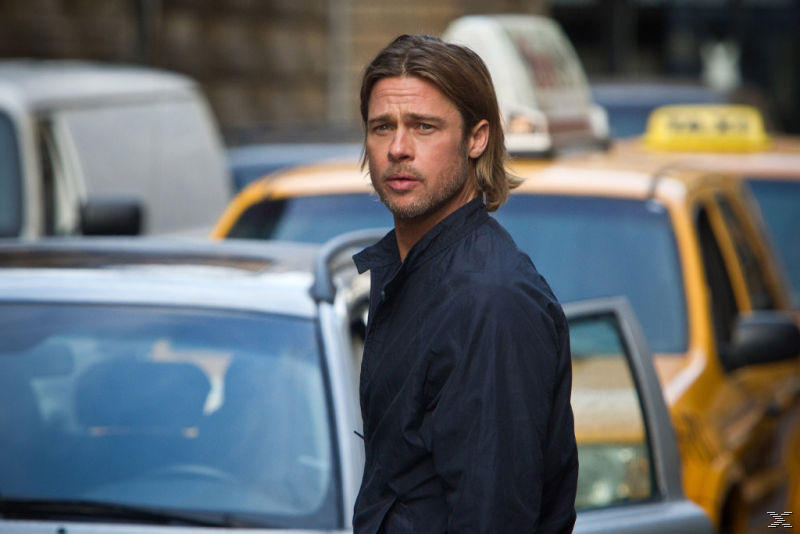 Brad Pitt in schwarzer Jacke steht in der Nähe von Taxis. Er blickt nach links, Gebäude im Hintergrund.