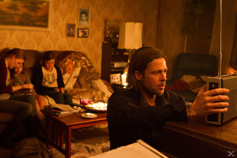 Brad Pitt hört in einem Raum Radio. Andere sitzen auf einem Sofa im schwach beleuchteten Hintergrund.