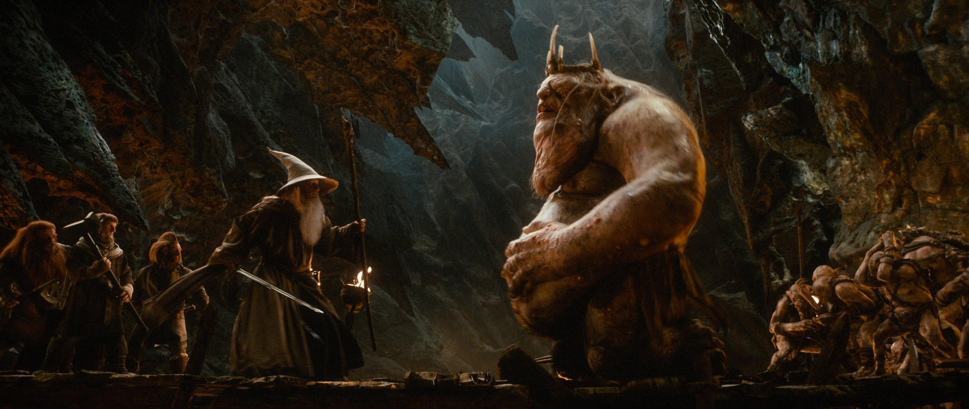 Gandalf und Zwerge stehen in einer Höhle einem großen Troll gegenüber.