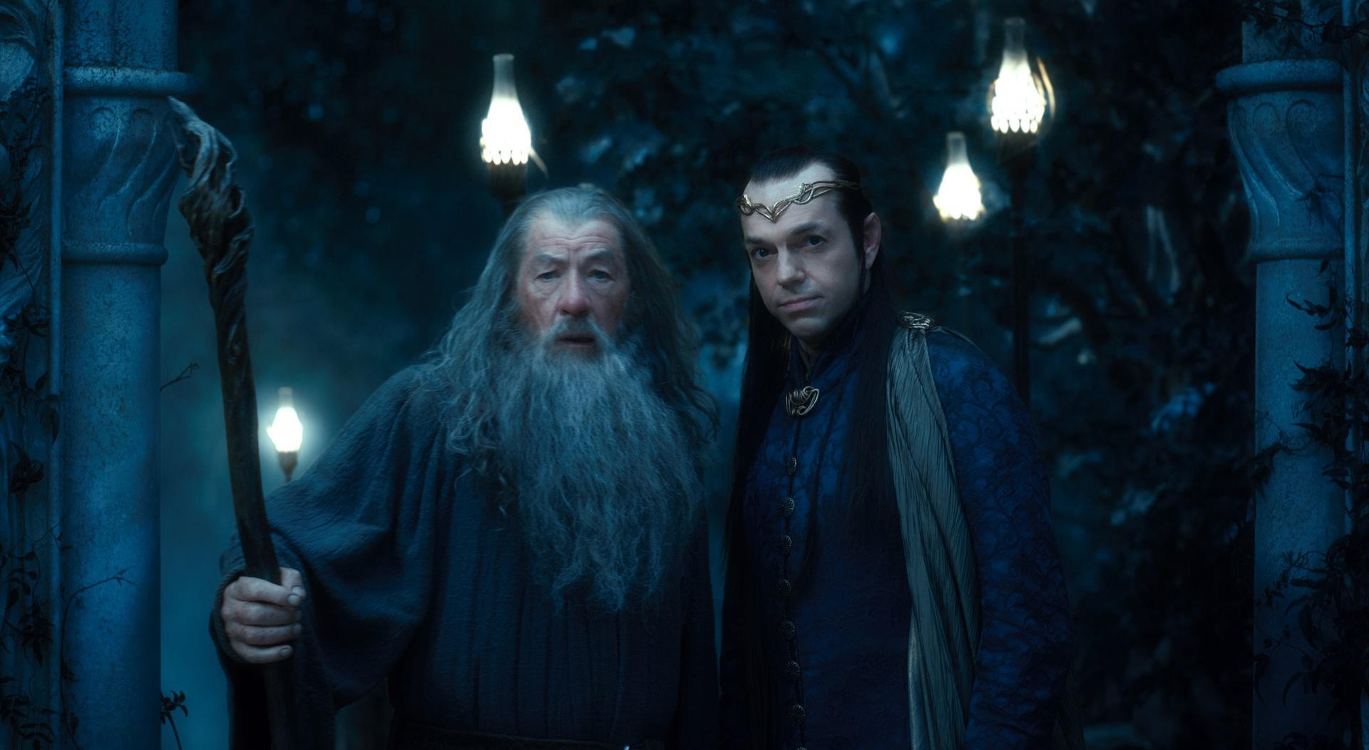 Gandalf und ein anderer Elf schauen in die Kamera. Bäume und Lichter sind im Hintergrund.