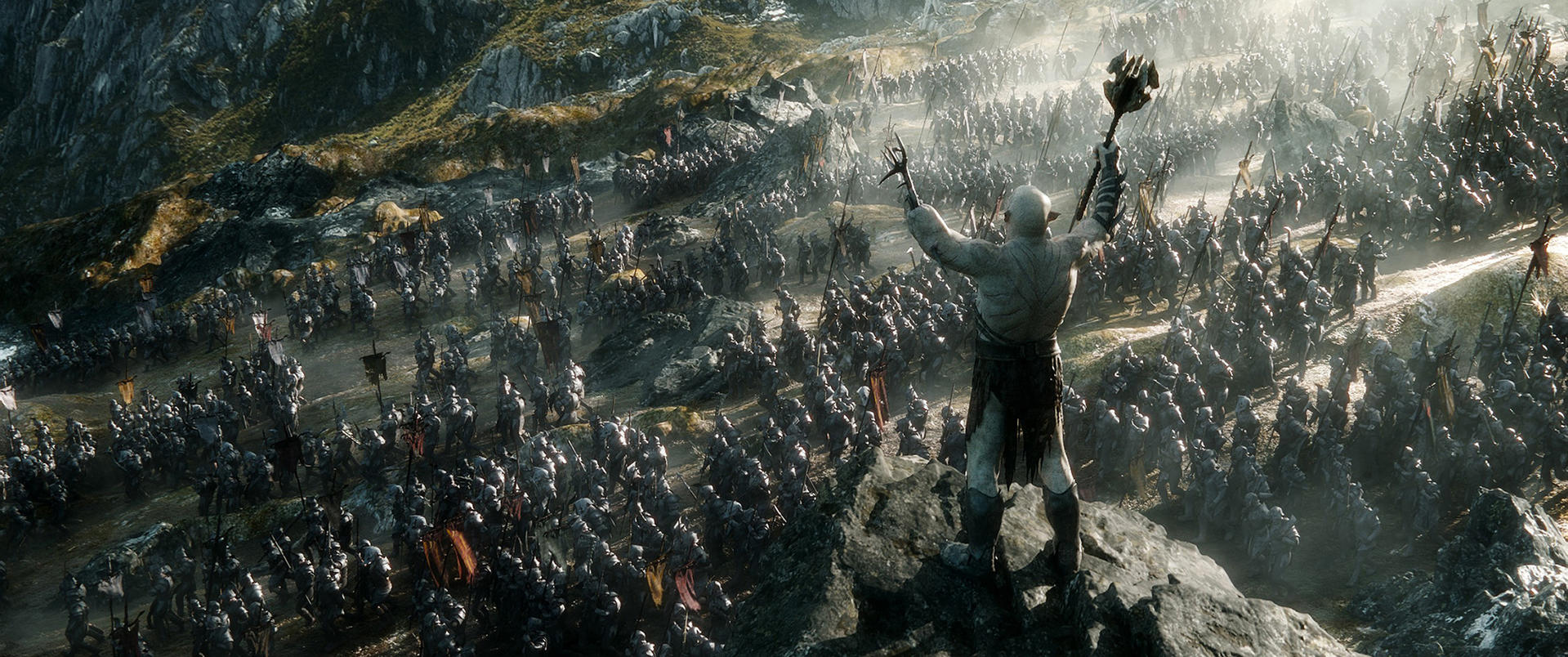 Ein Mann mit einer Waffe auf einem Hügel blickt über eine große Armee von Orks. Berge im Hintergrund.