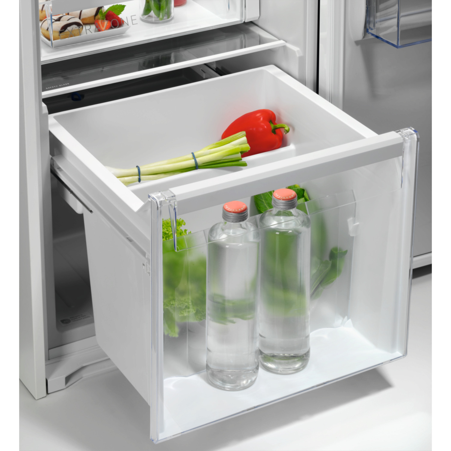Koelkastlade. Bevat waterflessen, sla en rode paprika. Transparante lade, wit interieur.