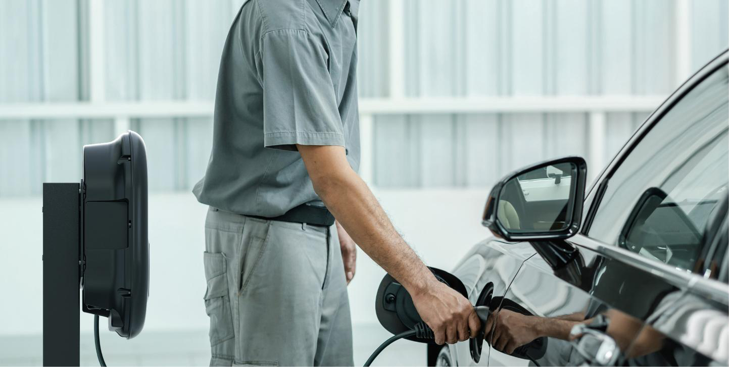 Person lädt ein Elektroauto an einer Ladestation auf. Das Auto ist schwarz. Die Station ist schwarz.