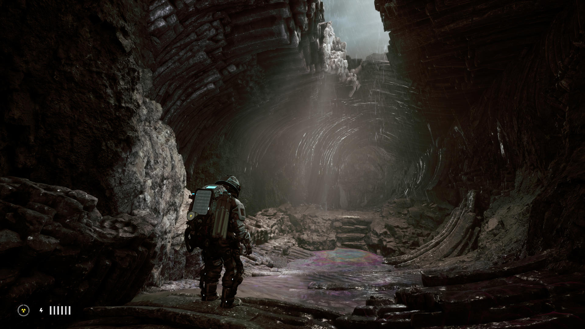 Eine Figur geht durch einen Steintunnel. Eine bunte Pfütze befindet sich auf dem Boden.