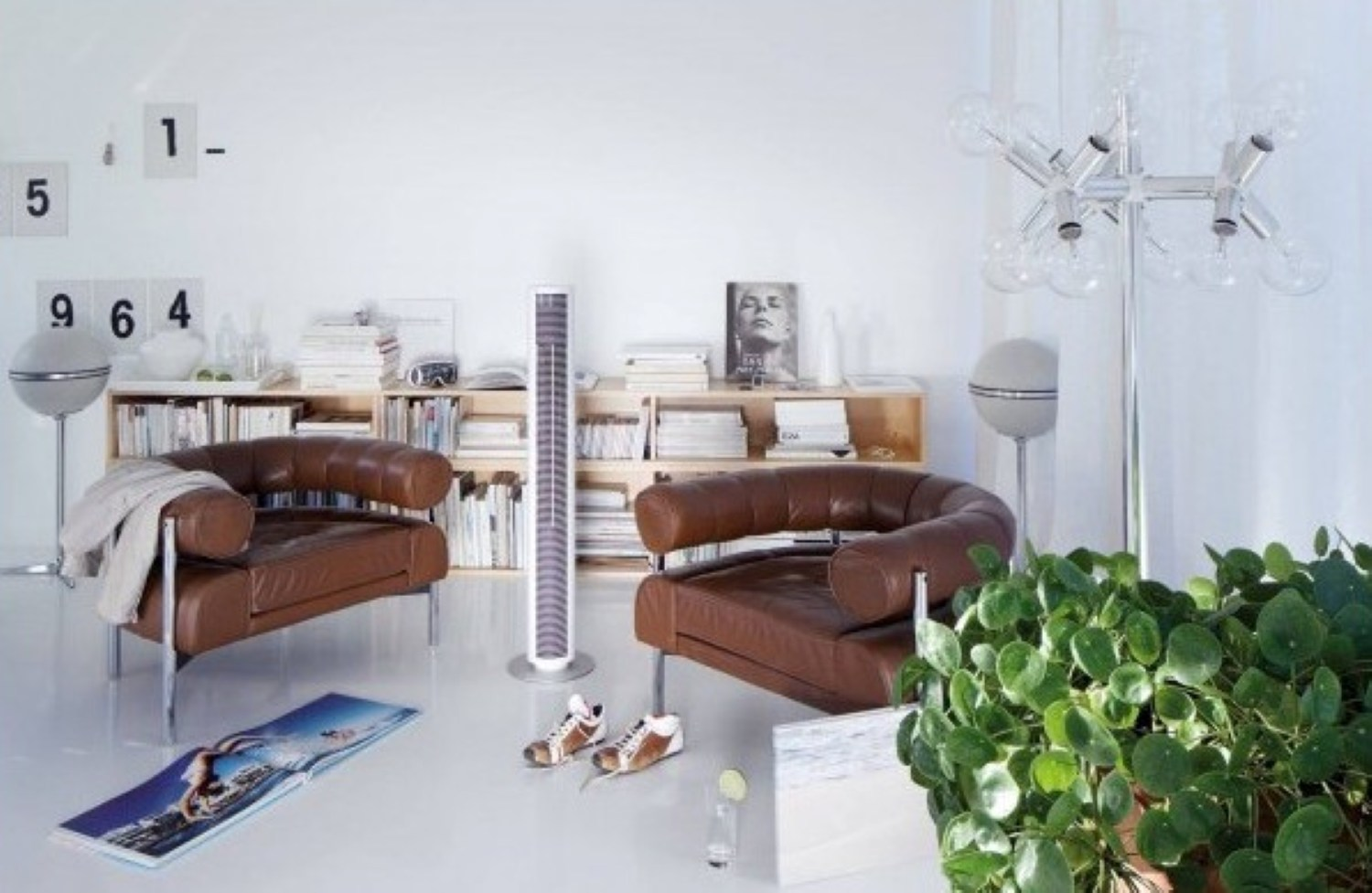 Scena w salonie. Brązowe skórzane fotele, biały oczyszczacz powietrza i nowoczesna lampa.
