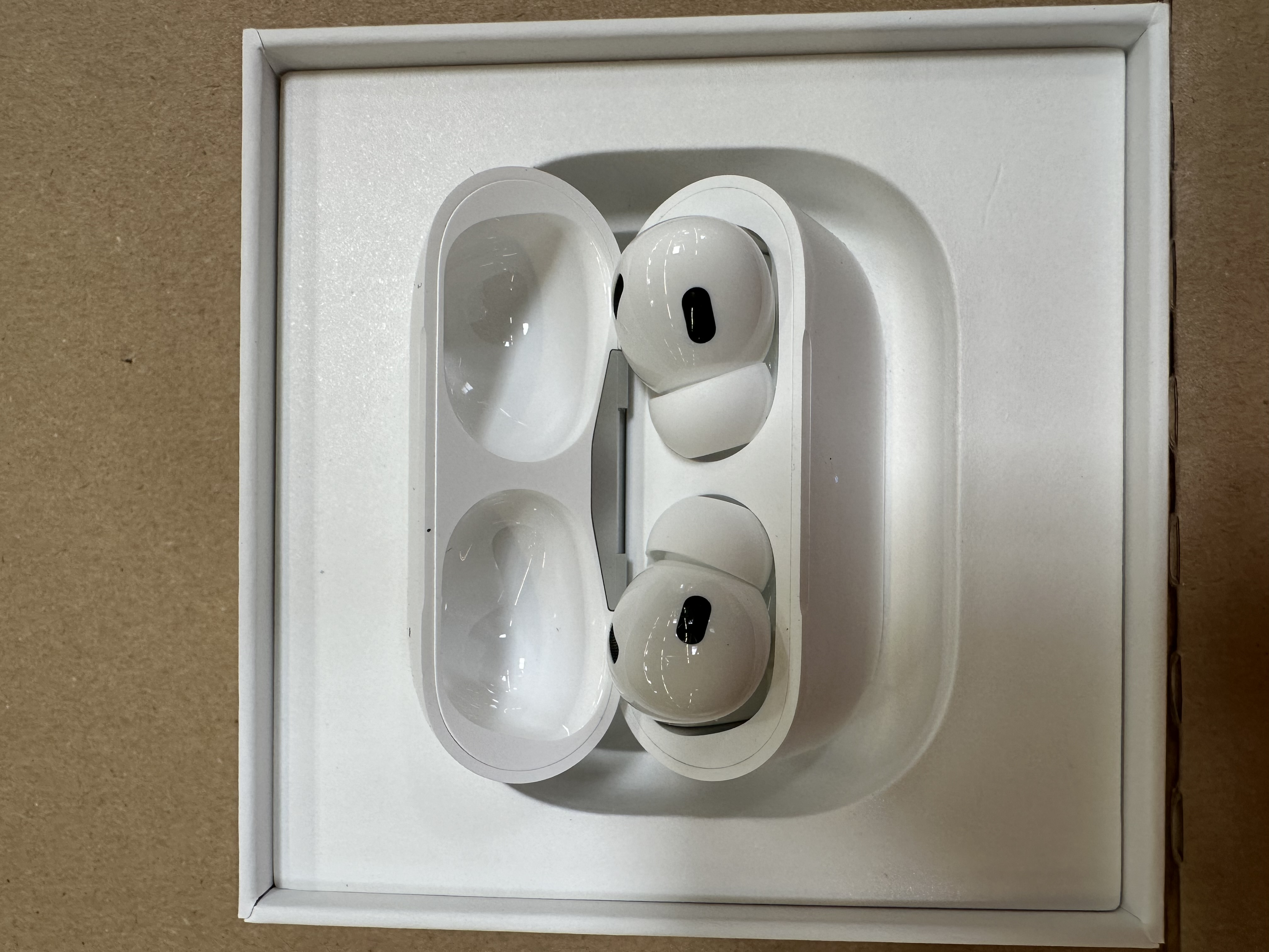 Białe AirPods Pro w białym etui, otwarte. Słuchawki są białe, z czarnymi detalami.