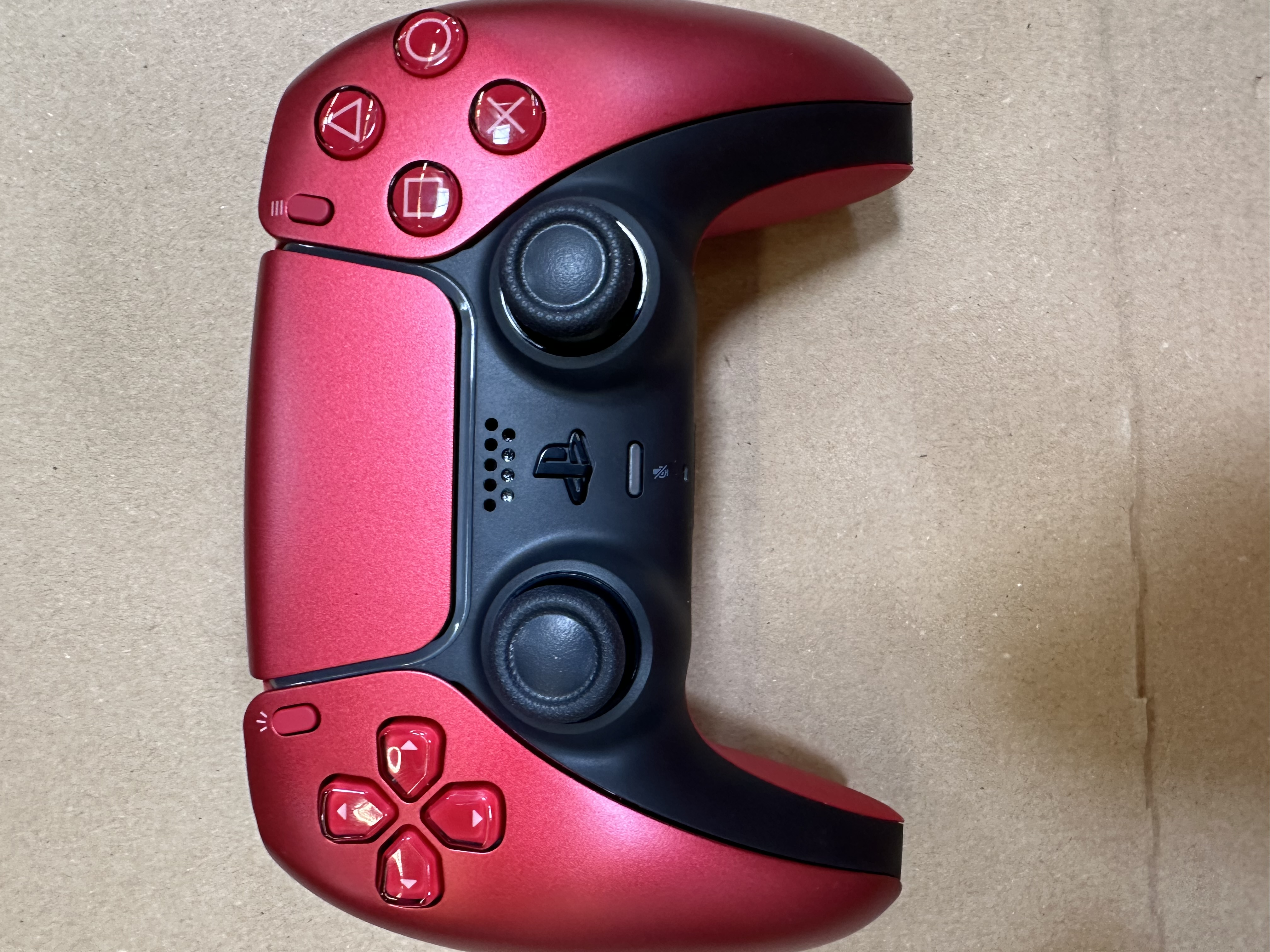 Czerwono-czarny kontroler gier na brązowej powierzchni. Widoczne przyciski i joysticki.