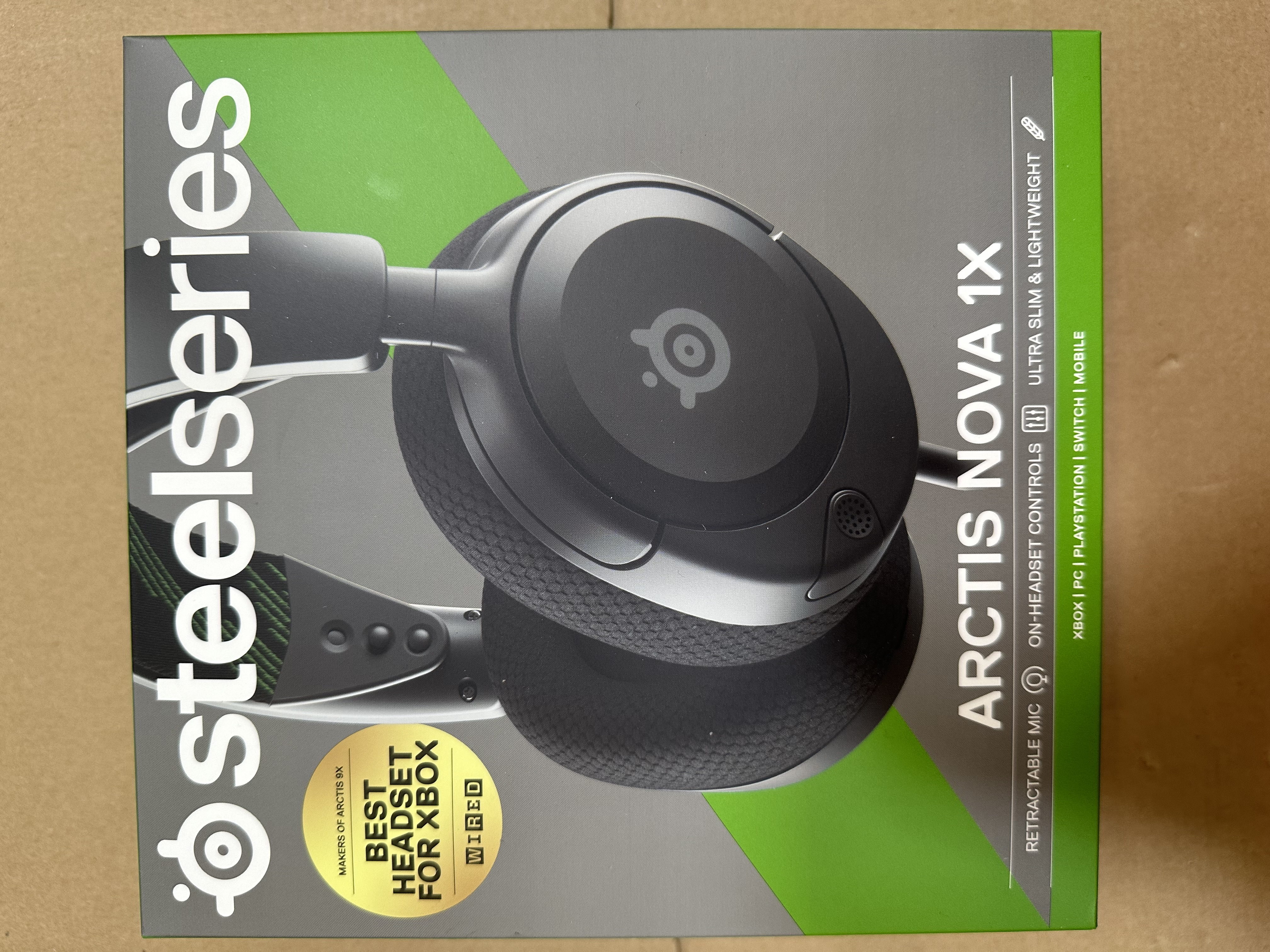 Czarny zestaw słuchawkowy do gier SteelSeries Arctis Nova 1X w pudełku. Tekst na pudełku opisuje jego funkcje.