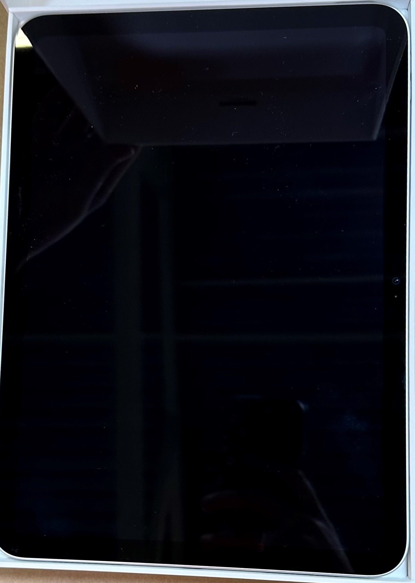 Czarny ekran tabletu w białym pudełku. Ekran odbija pokój i światła.