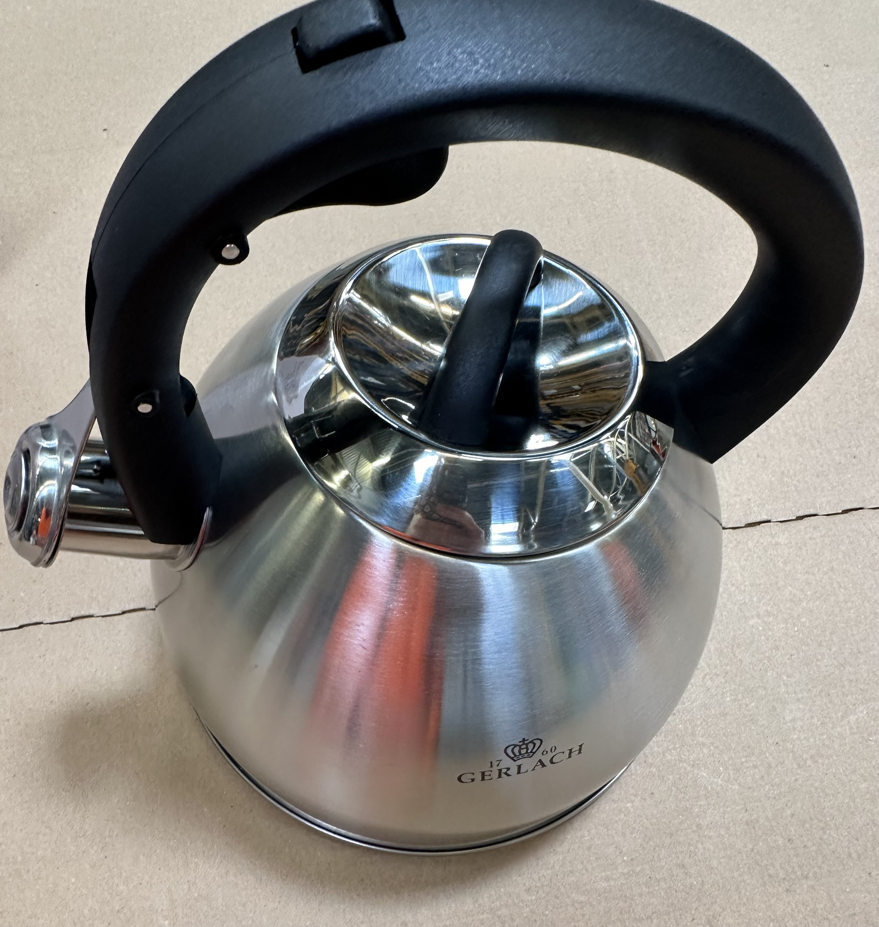 Czajnik ze stali nierdzewnej z czarnym uchwytem na kartonowej powierzchni.